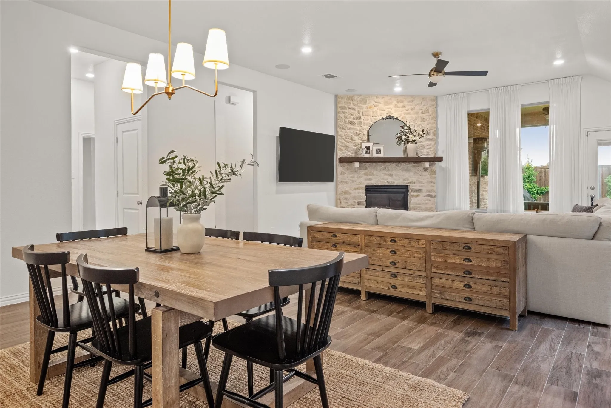 Open-concept living space featuring wood-finish flooring, a stone-faced fireplace with a mantel, and a gold-finish chandelier