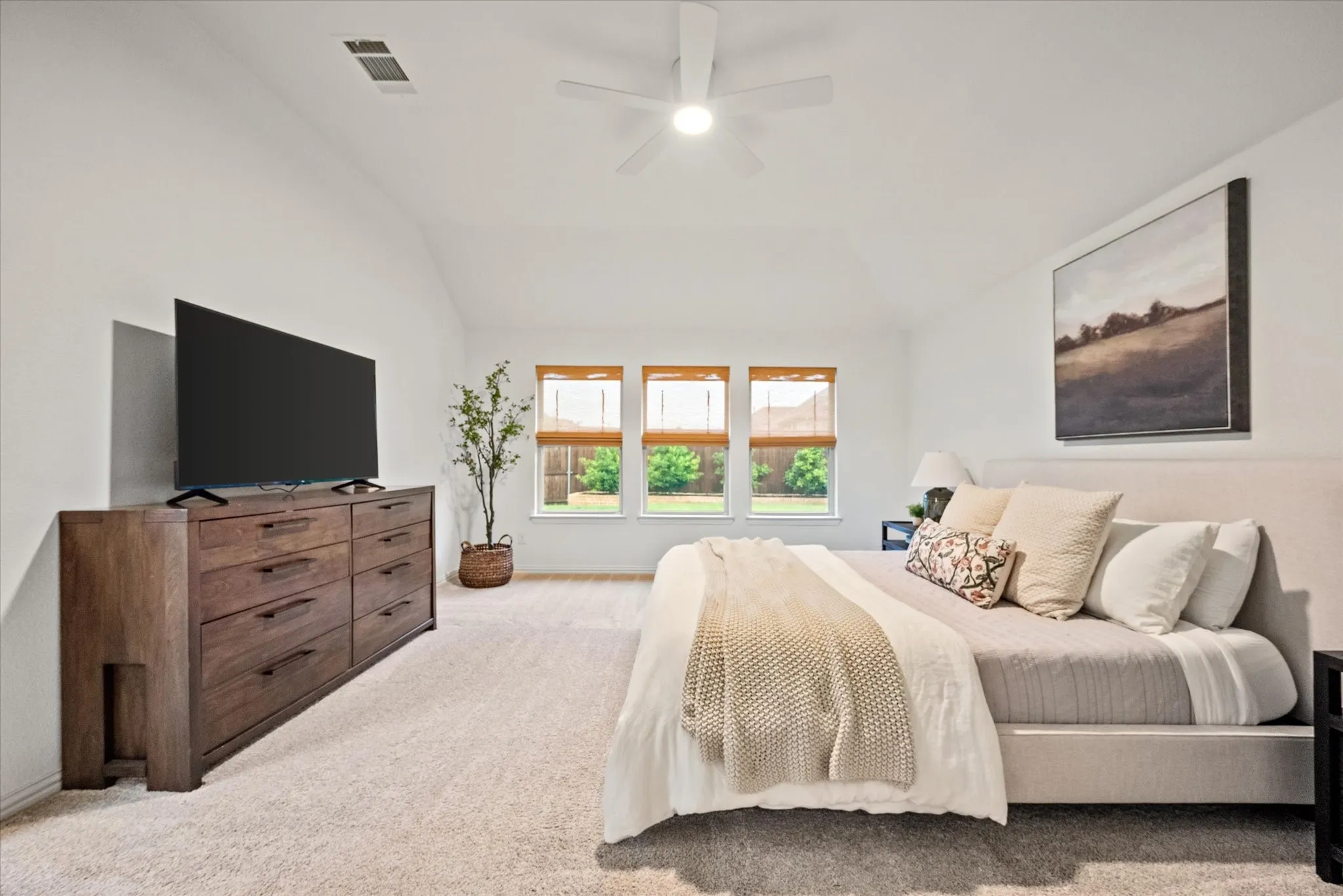 Vaulted ceiling, ceiling fan with integrated lighting, three windows with natural light, wall-to-wall carpeting, and neutral color palette