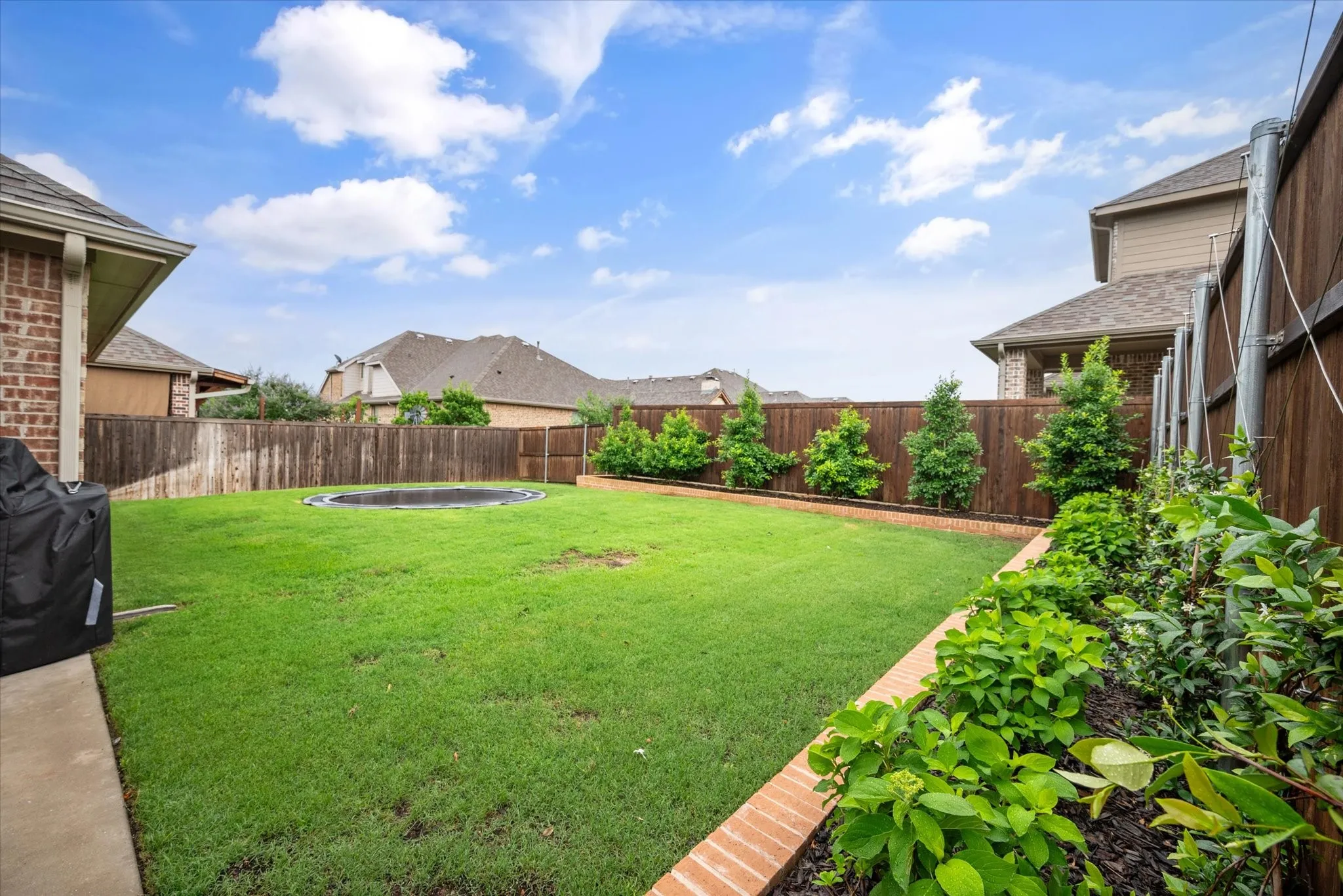 Expansive backyard with a manicured lawn, wood fencing, and a brick-edged planting bed with established greenery