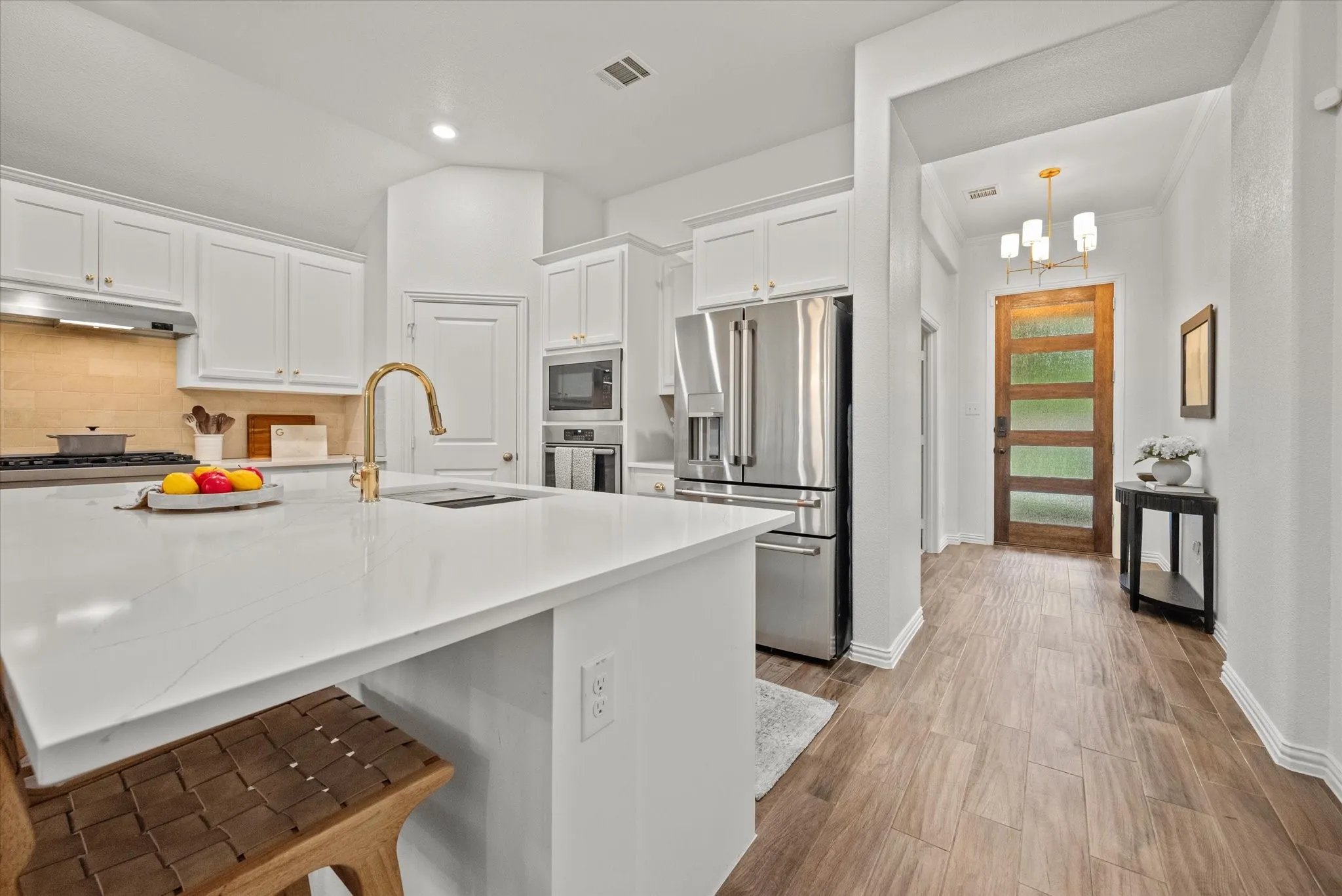 Kitchen featuring white cabinetry, stainless steel appliances, a large island with a surface-mounted sink, and a gold-tone faucet