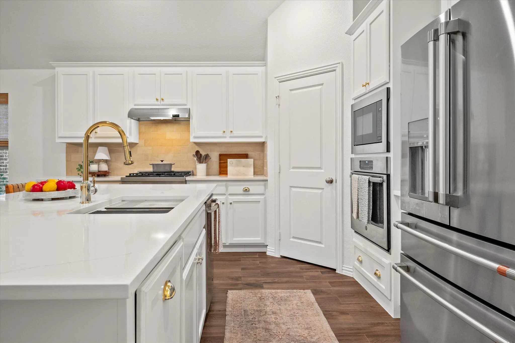 White cabinetry, stainless steel appliances, a large center island, gold-finish hardware, and wood-finish flooring