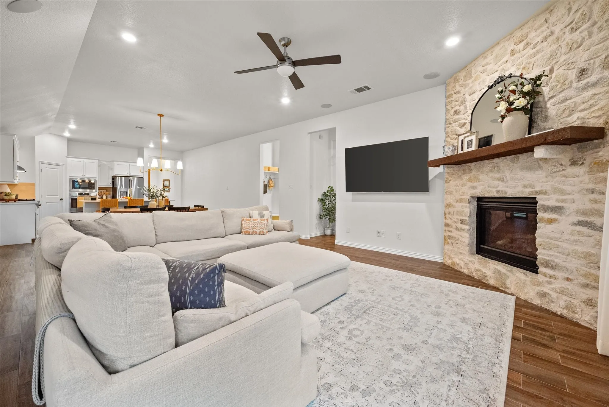 Stone-clad fireplace with a wood mantel, wood-finish flooring, recessed lighting, and a ceiling fan