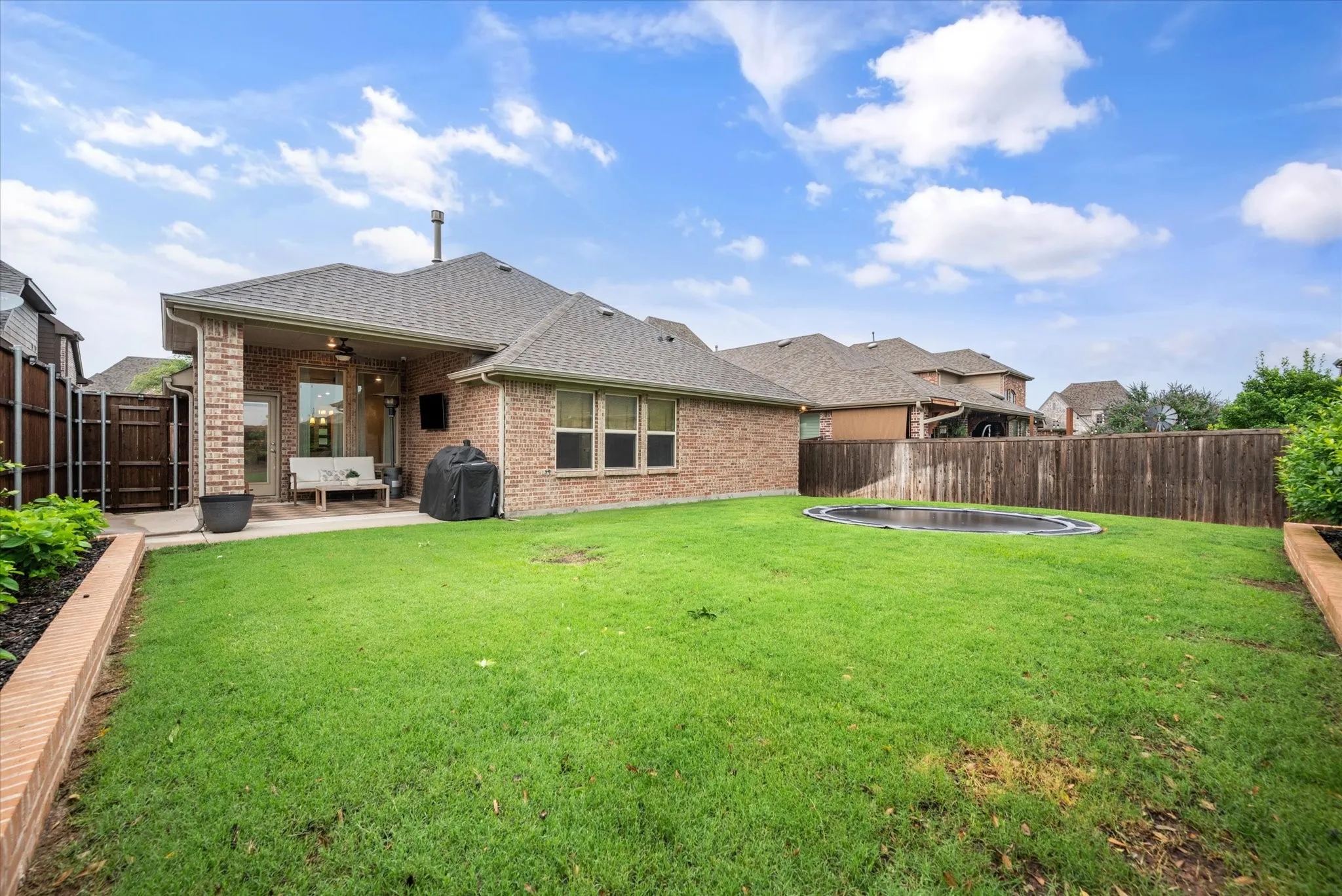 Expansive green lawn with a covered patio, brick exterior, and a wood privacy fence