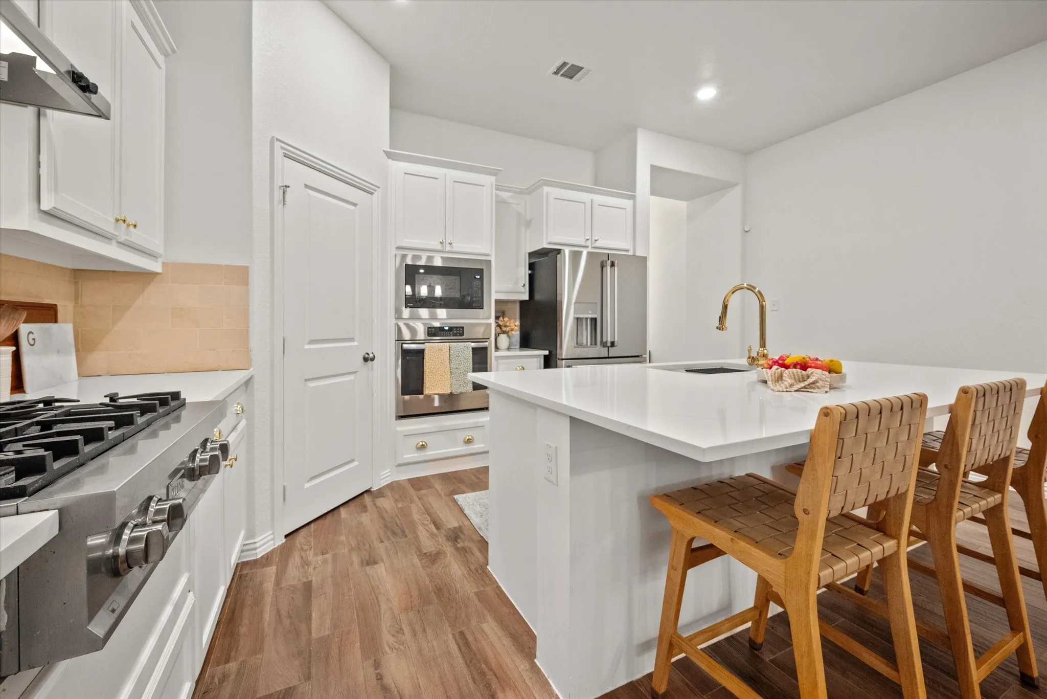 White cabinetry with gold-finish hardware, built-in stainless steel appliances, wood-finish flooring, and a kitchen island with a gold-finish faucet