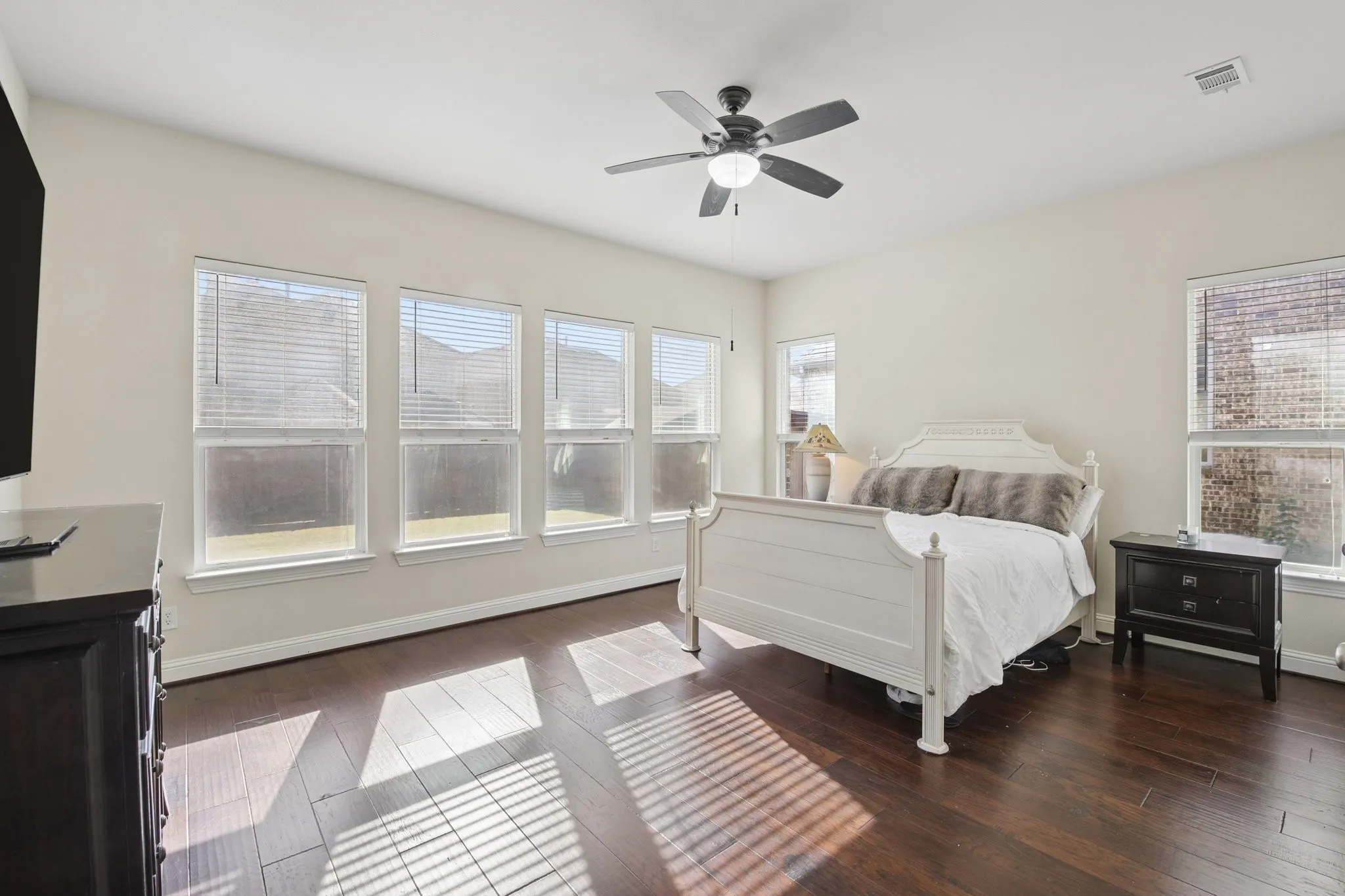 Spacious room with dark wood-finish flooring, multiple windows, and a ceiling fan with integrated lighting