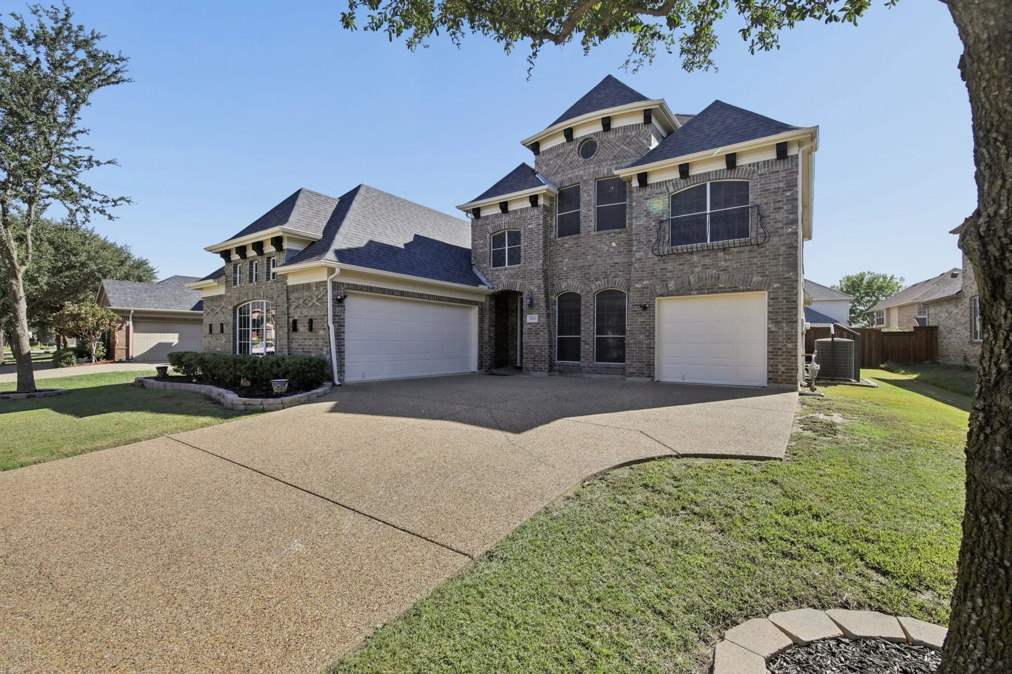 Brick exterior with decorative stone accents, multiple garage bays, and a large aggregate driveway