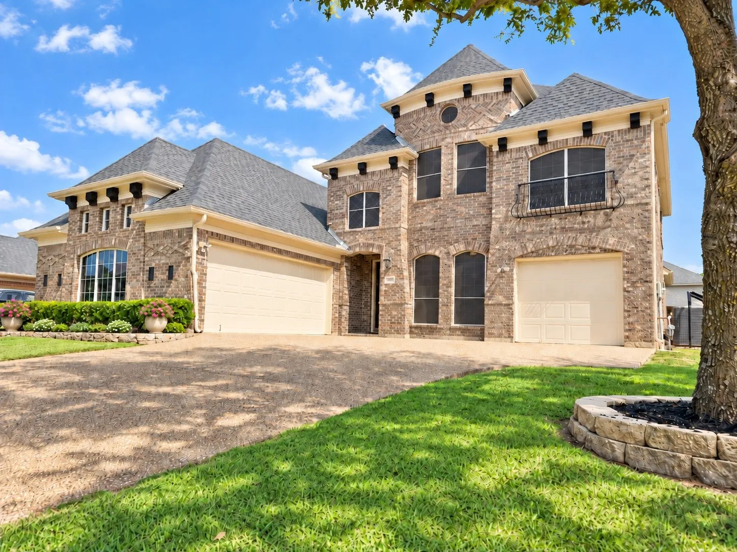 Freshly painted brick residence featuring multiple dormers, a balcony, and two garage bays