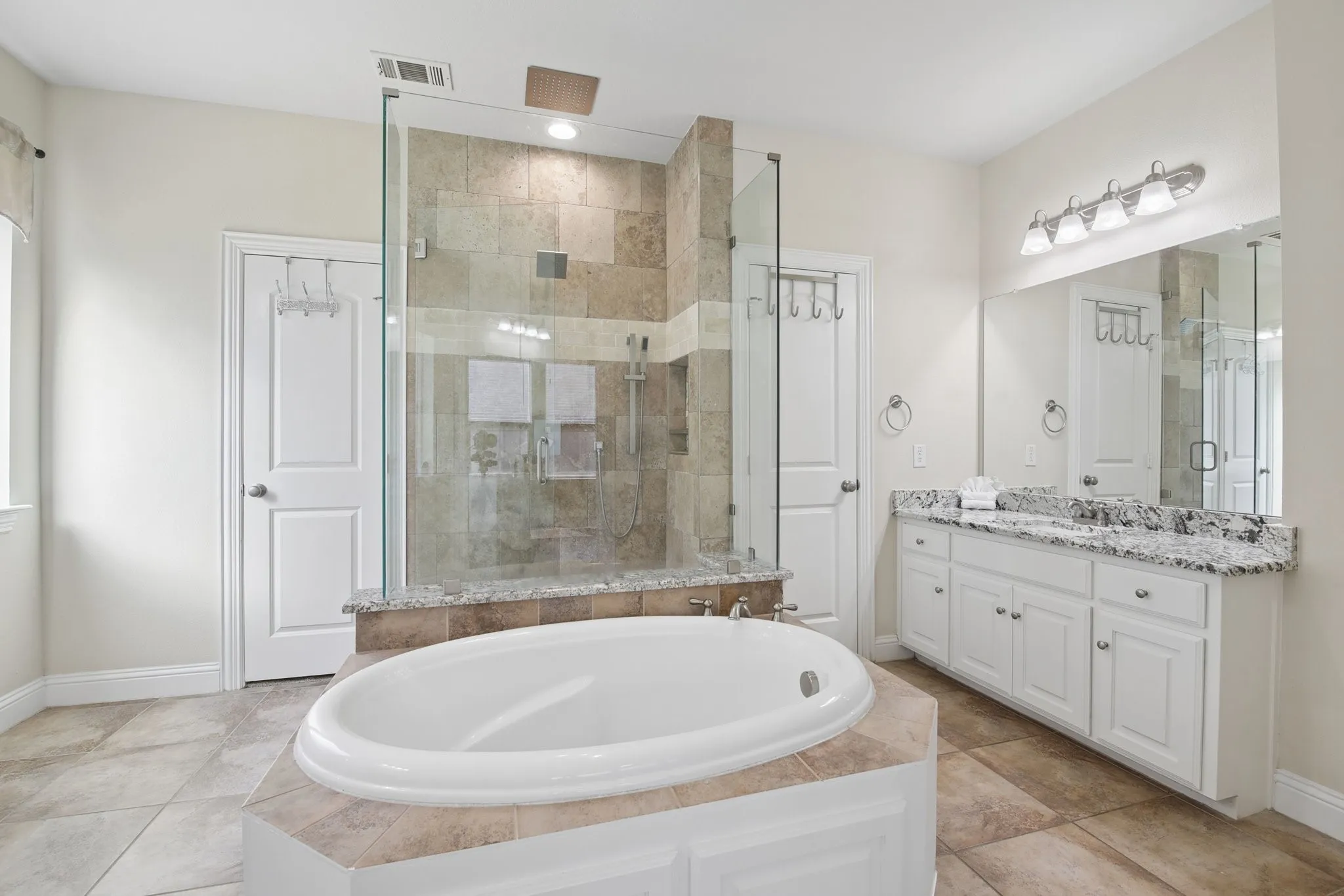 Built-in soaking tub with tiled surround, walk-in shower with glass enclosure, dual vanity with granite countertops, and tile flooring