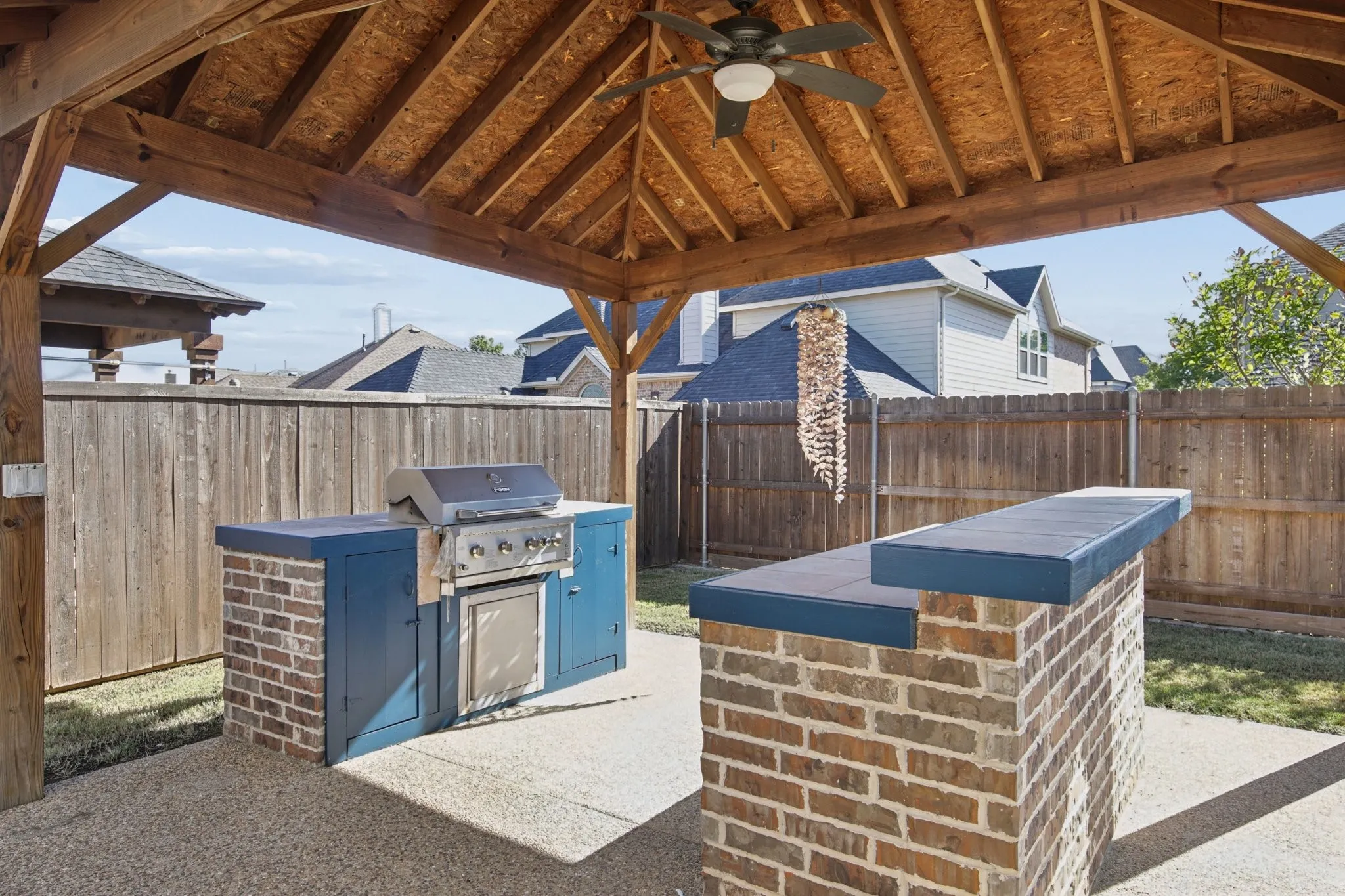 Covered outdoor patio with a ceiling fan, a built-in brick and cabinet grill station, and a brick bar with a countertop