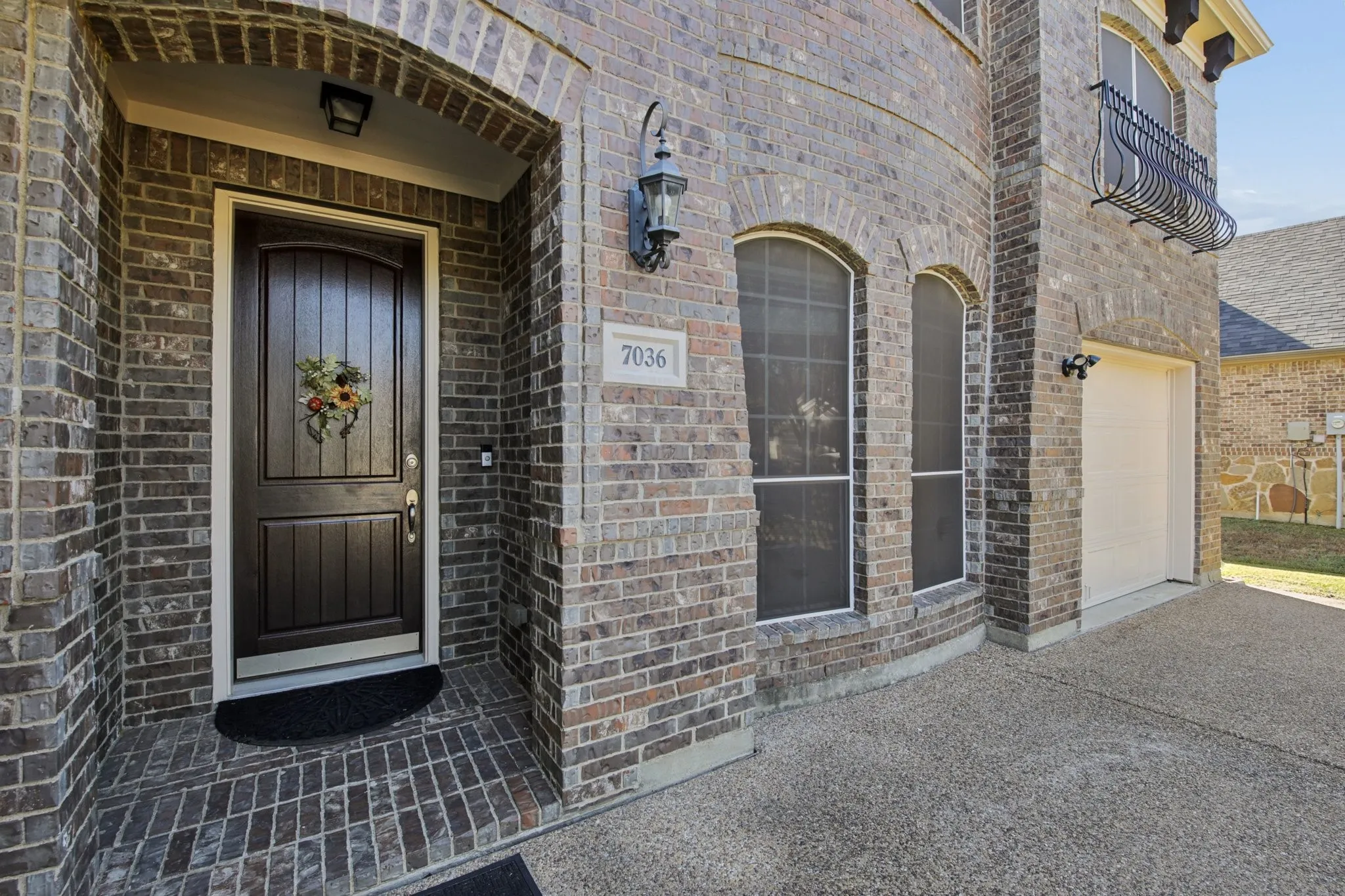 Brick exterior with arched entryway, arched windows, and a decorative wrought iron balcony
