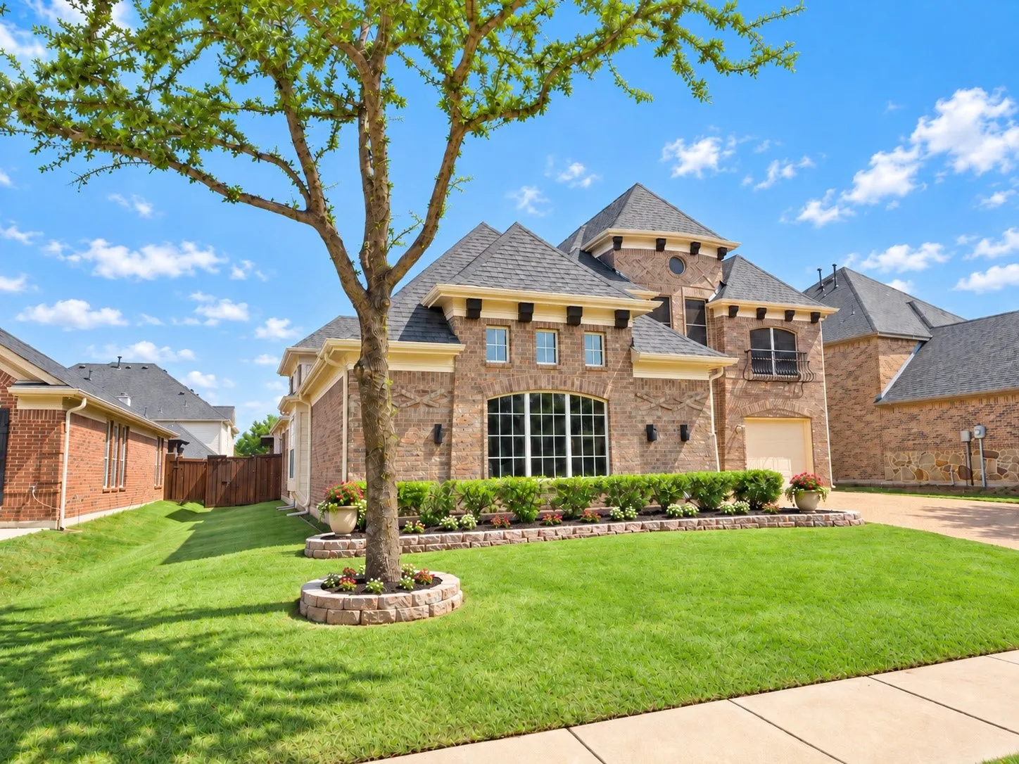 Brick facade with stone accents, multiple gabled rooflines, arched window, integrated garage, and a landscaped front yard with a mature tree