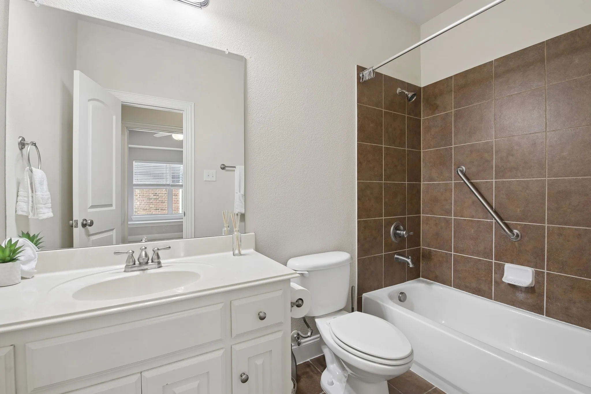 1st Floor Bathroom featuring a white vanity with an integrated sink, chrome faucet, a toilet, and a tiled shower-bathtub combination with a grab bar