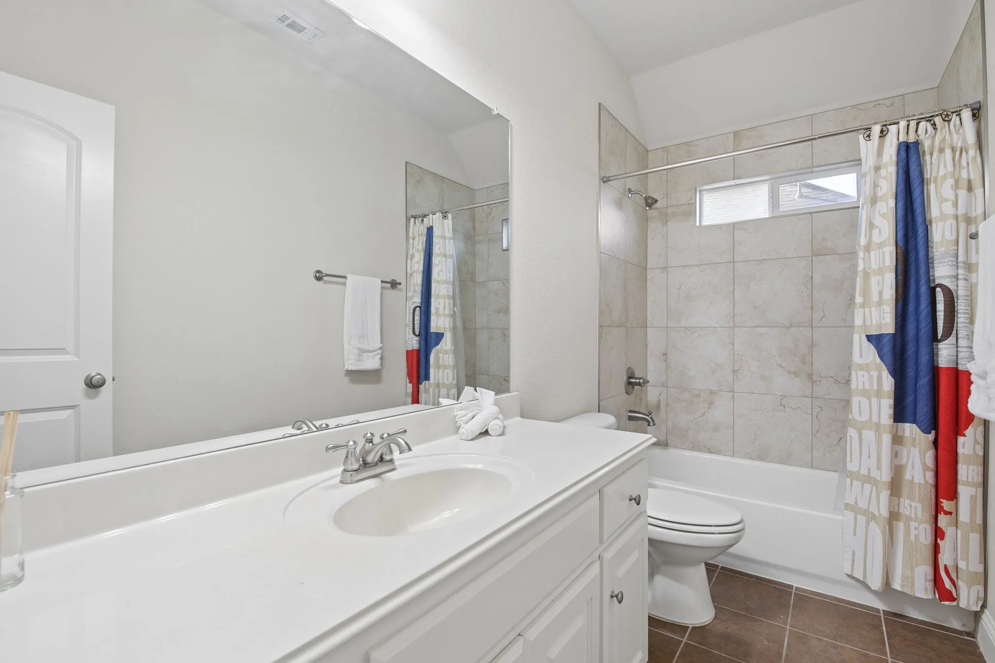 Upstairs with white vanity with integrated sink and chrome faucet, full-width mirror, tile flooring, and a shower-tub combination with tile surround and transom window