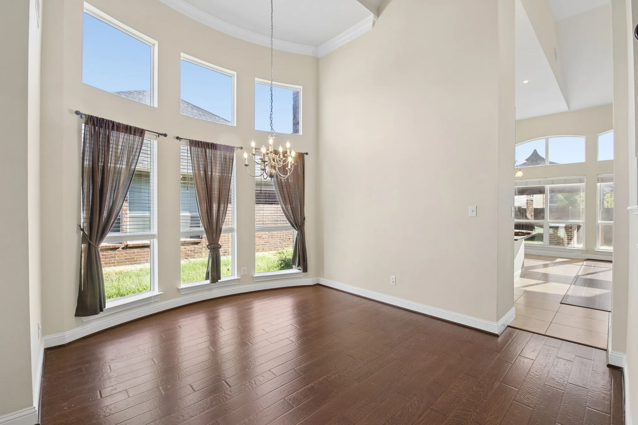 Curved wall of windows, high ceilings, wood-finish flooring, and a decorative chandelier