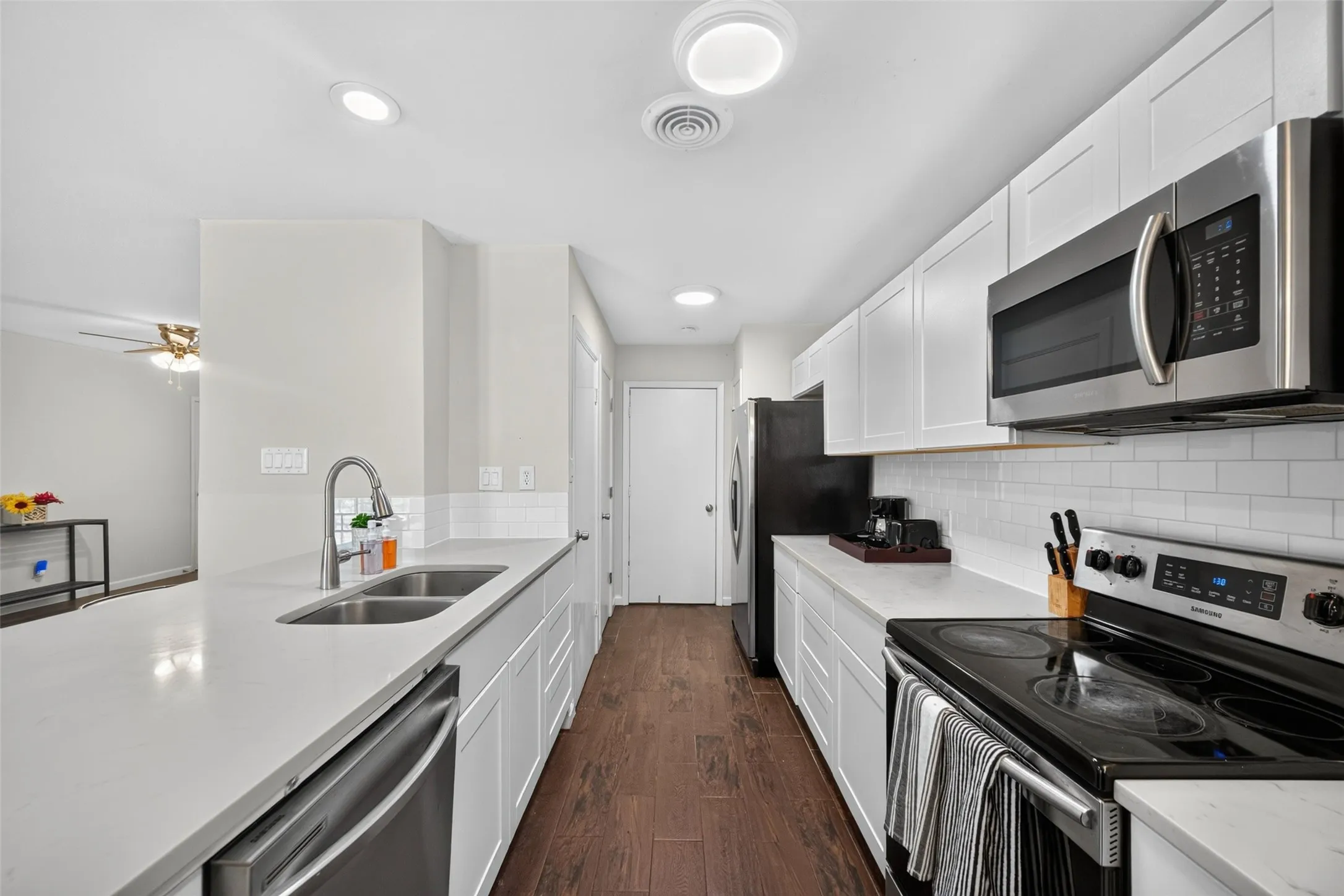 Sleek kitchen with white cabinetry, stainless steel appliances, light-toned countertops, and wood-finish flooring