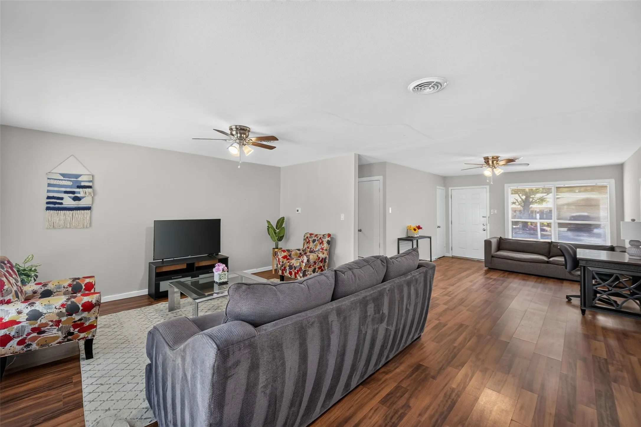 Open-concept living area featuring wood-finish flooring, light gray wall paint, and multiple ceiling fans