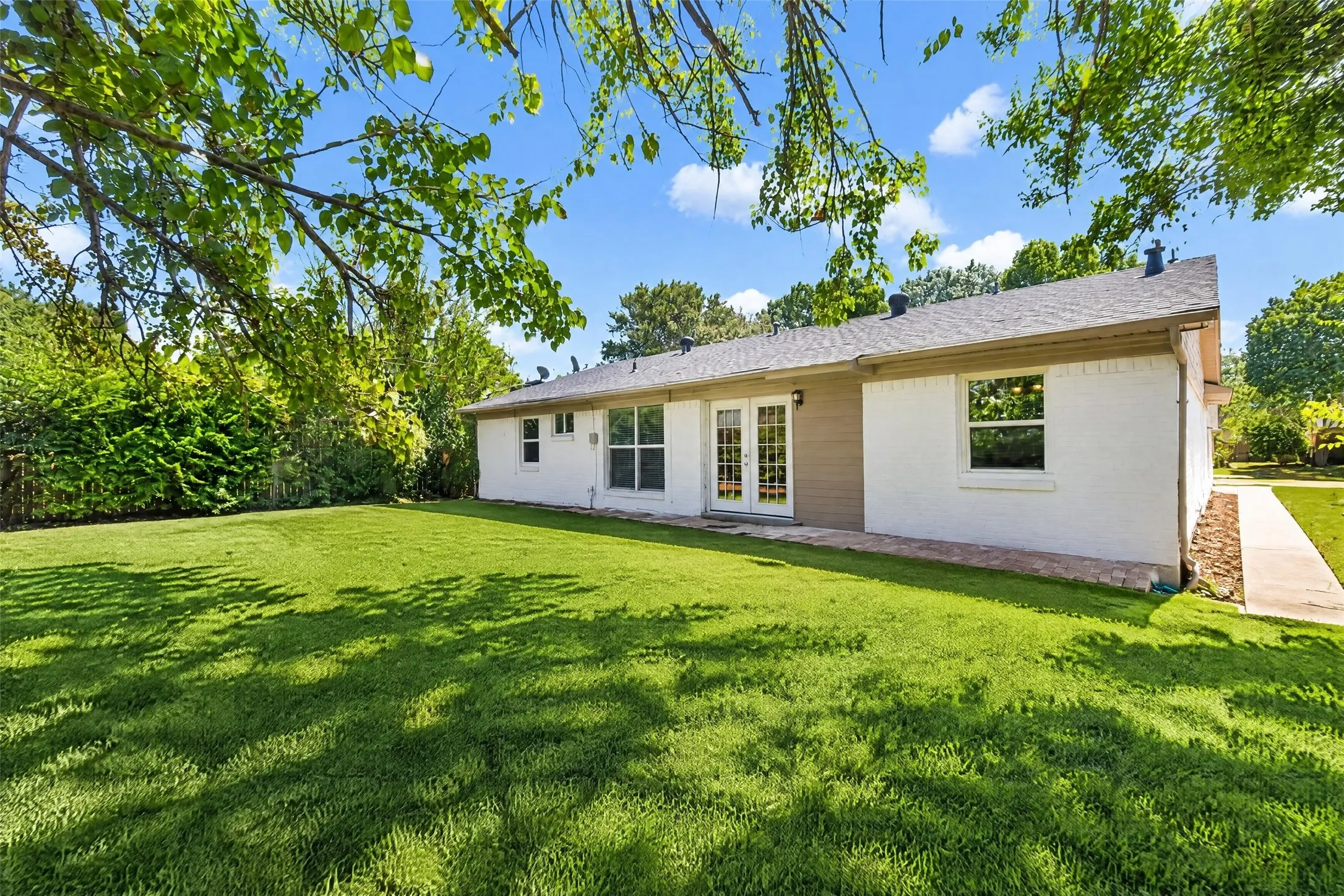 Expansive lawn with mature landscaping, white brick exterior, double glass panel doors, and a concrete pathway