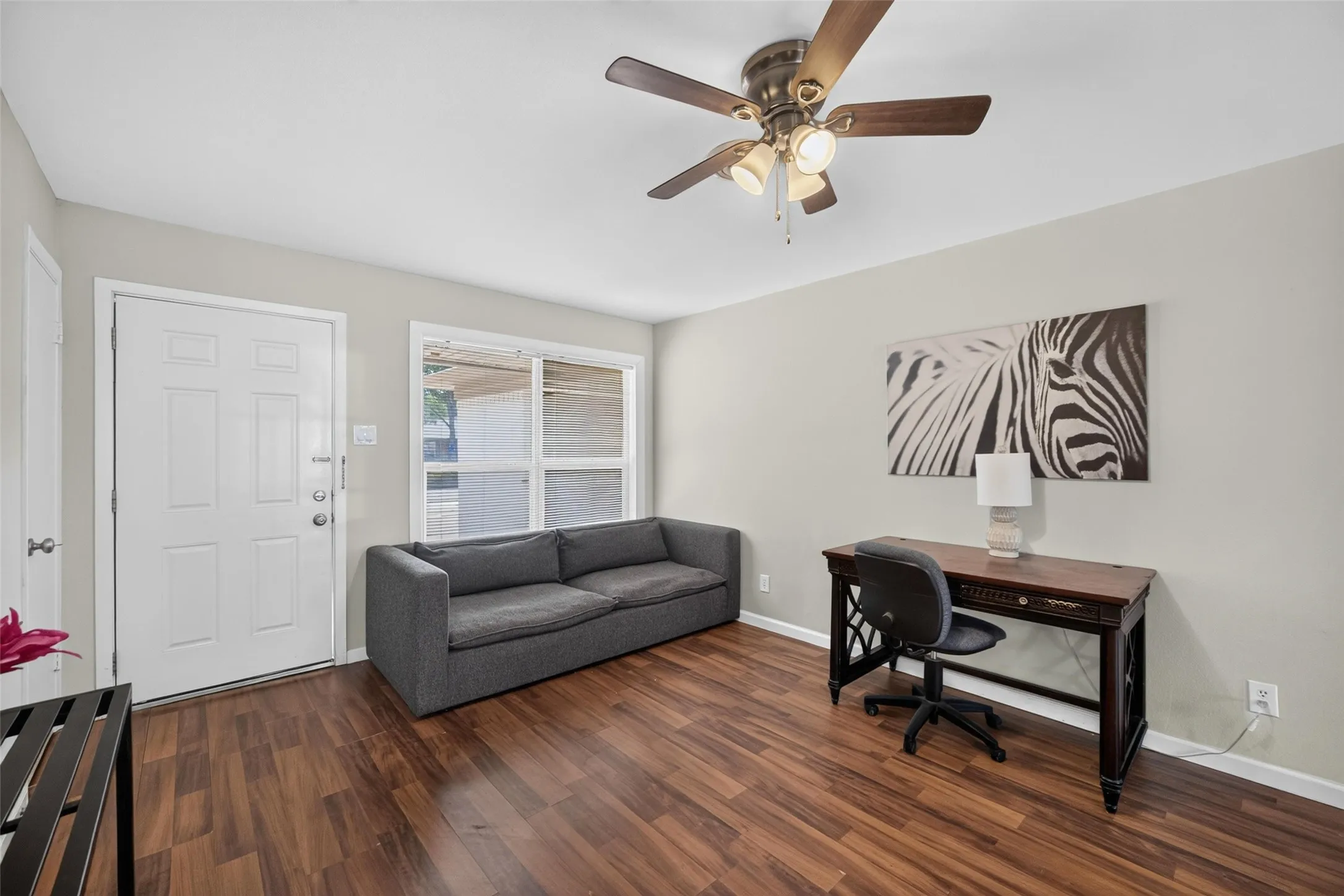 Wood-finish flooring, white paneled entry door, ceiling fan with integrated lighting, and a large window