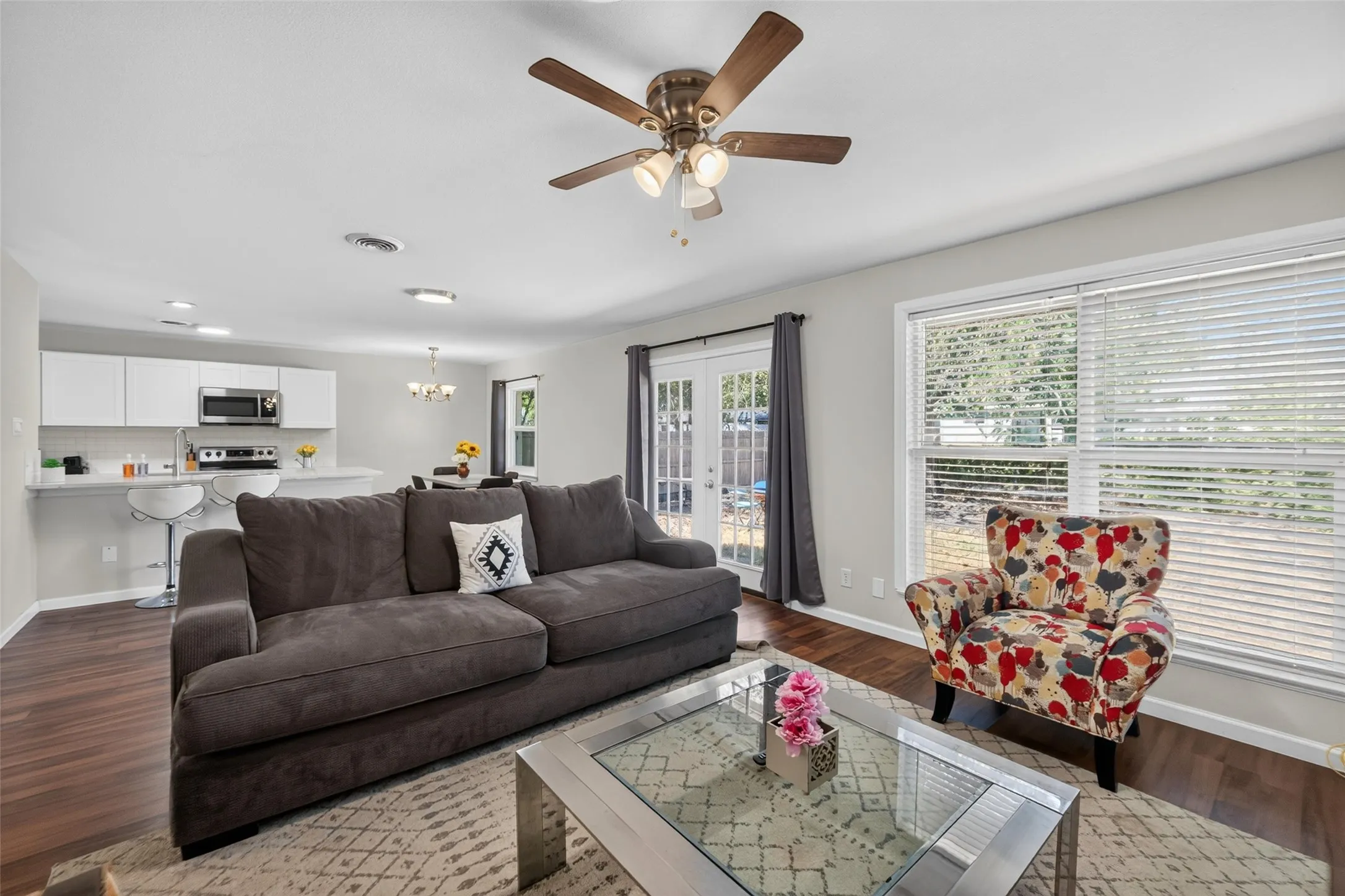 Open concept living area featuring wood-finish flooring, a ceiling fan, and large windows with blinds