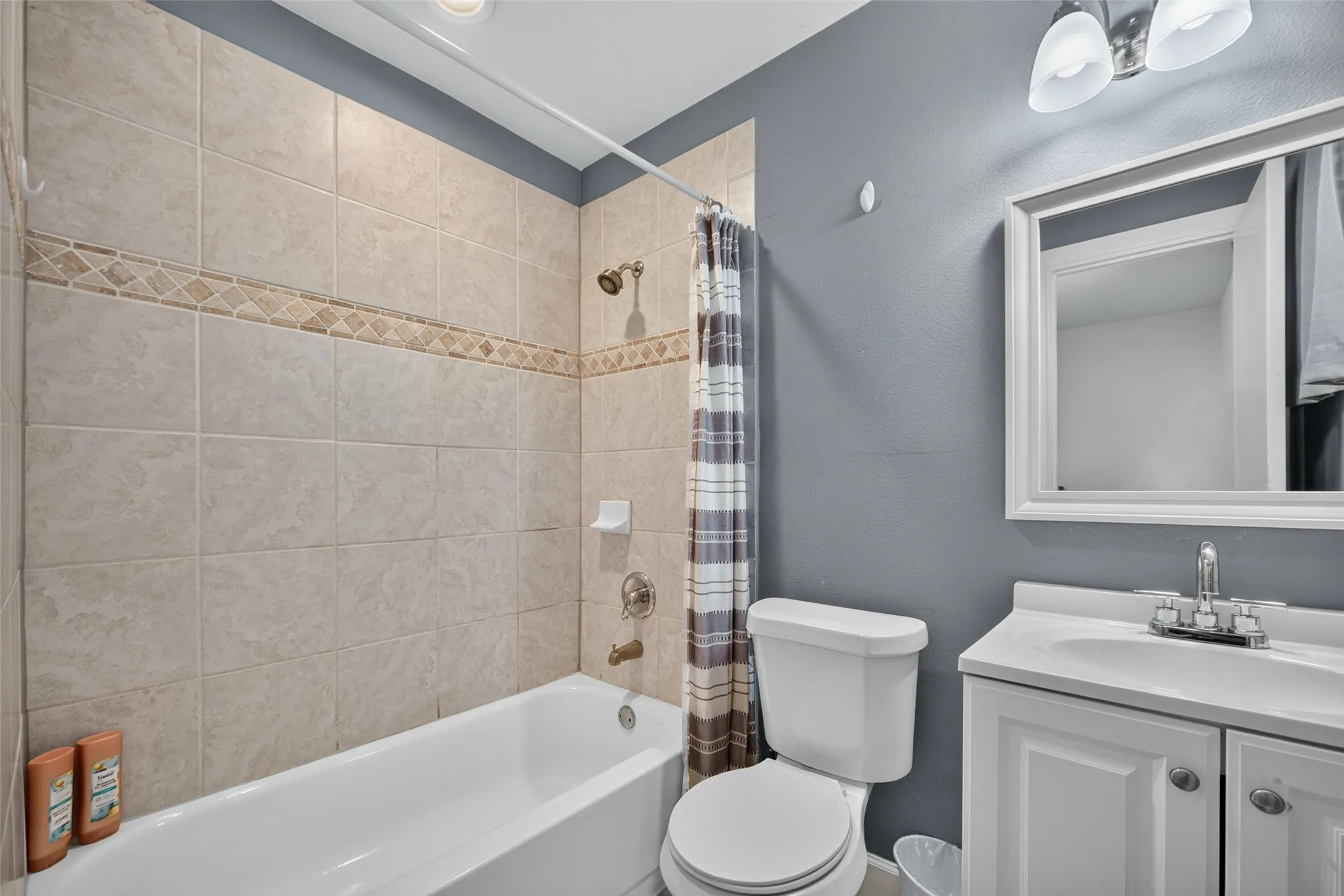 Full bathroom featuring a white vanity with a single sink, an integrated bathtub with a shower, and tile surround with a decorative accent band