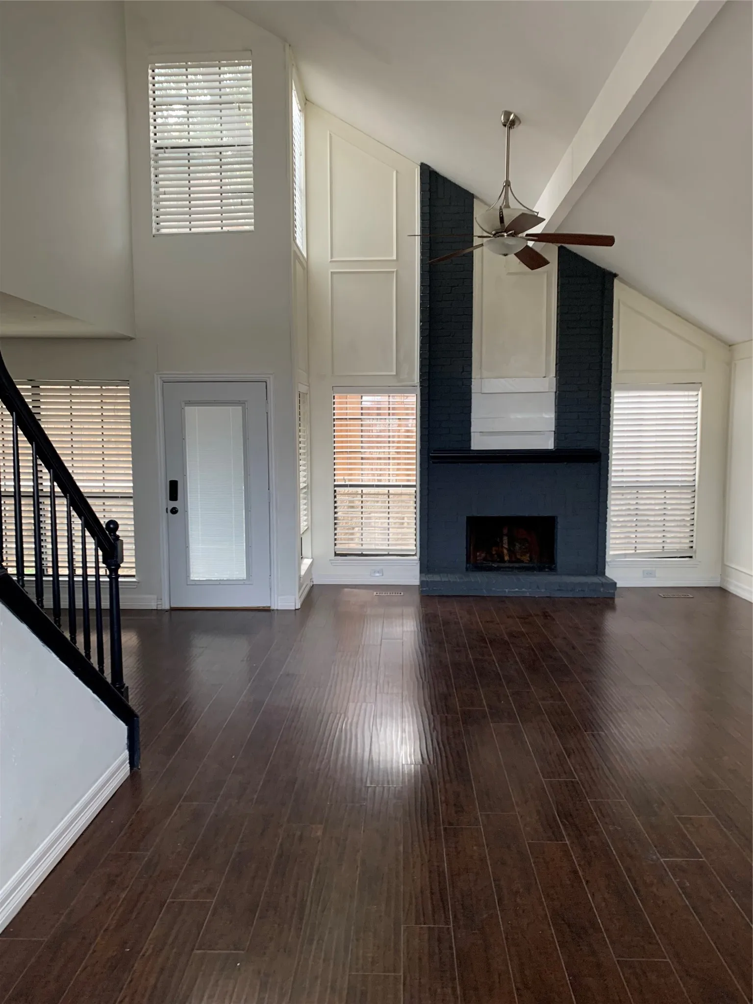 Unfurnished living room featuring dark hardwood / wood-style flooring, high vaulted ceiling, ceiling fan, and a fireplace