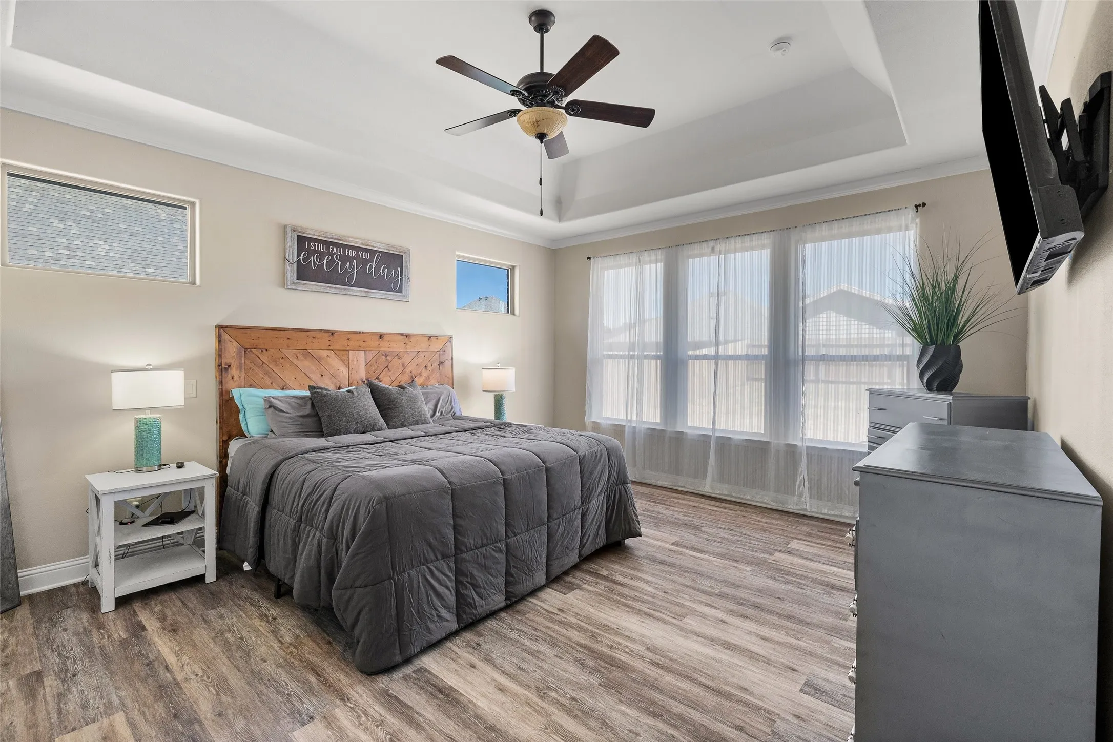 Tray ceiling with crown molding, wood-finish flooring, ceiling fan, transom windows, and a multi-pane window