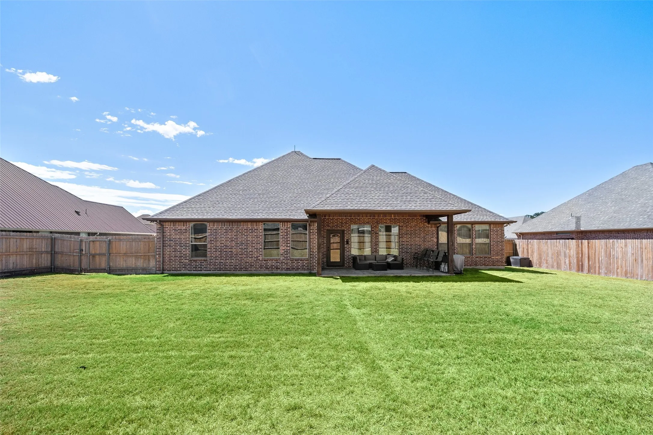 Expansive green lawn, brick exterior, covered patio, privacy fencing, and a shingled roof