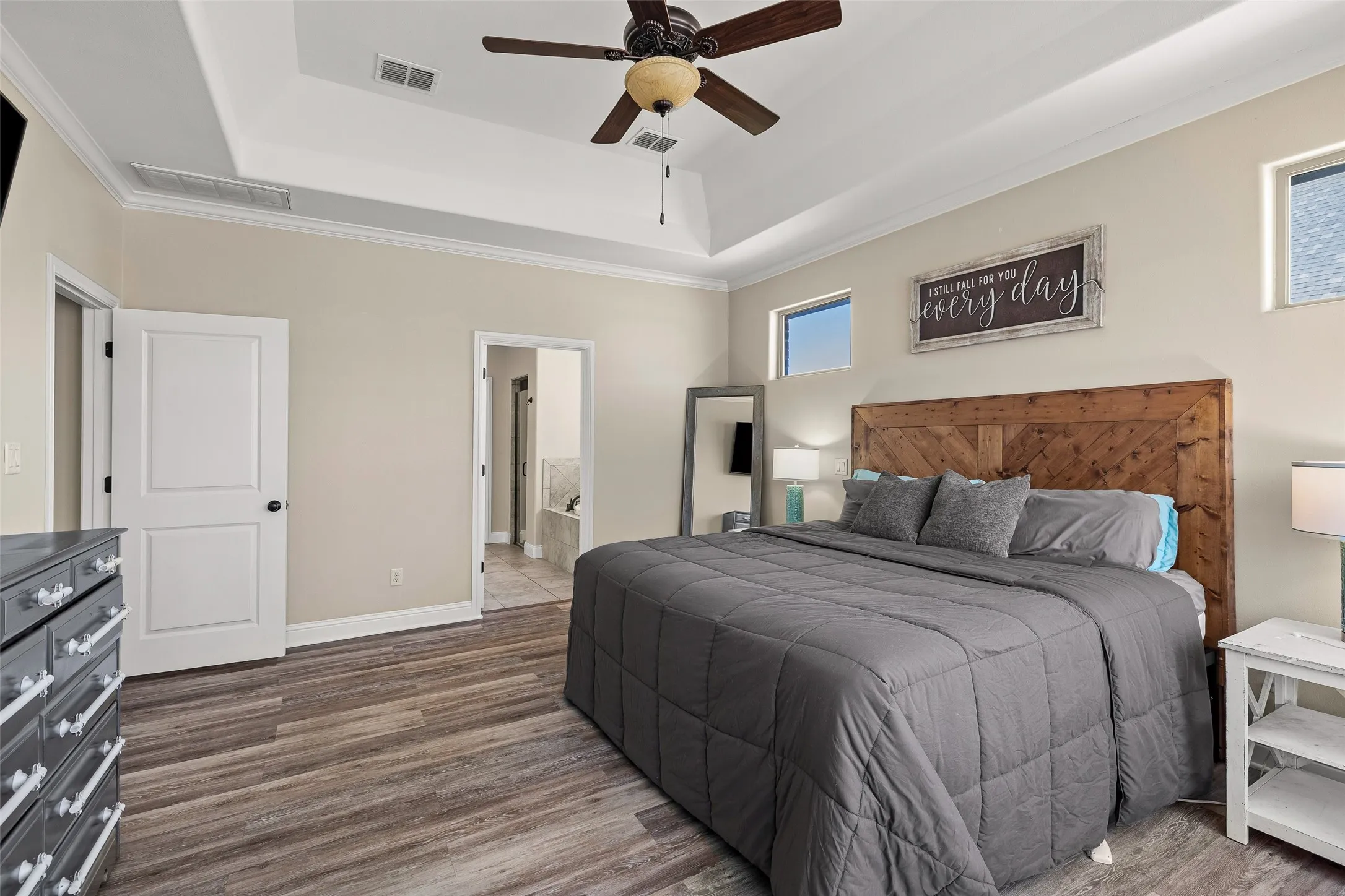 Tray ceiling with crown molding, wood-finish flooring, two high-set windows, white paneled doors, and a ceiling fan
