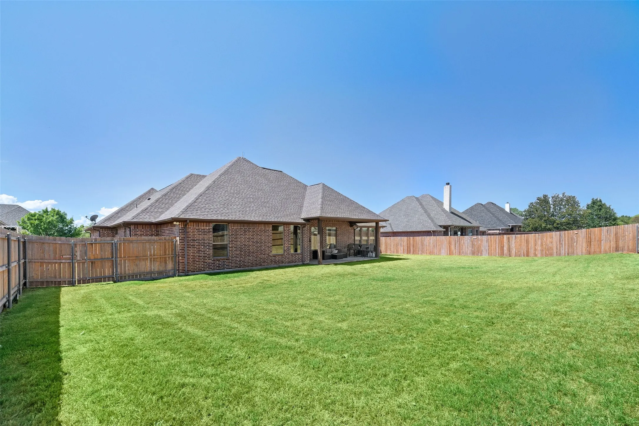 Expansive backyard featuring a manicured lawn, full privacy fencing, and a covered patio area