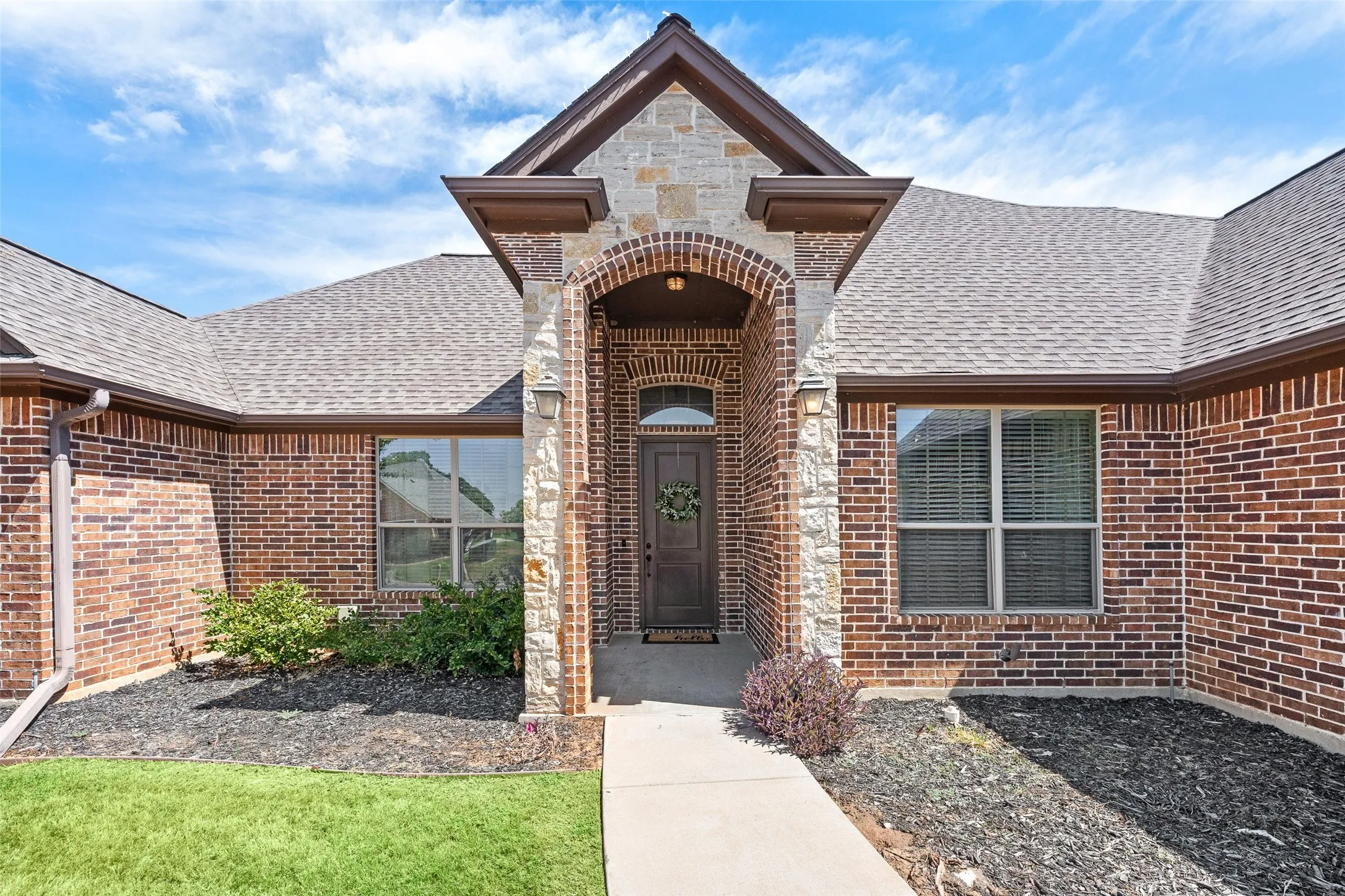 Brick and stone exterior with an arched entryway, covered porch, and mature landscaping