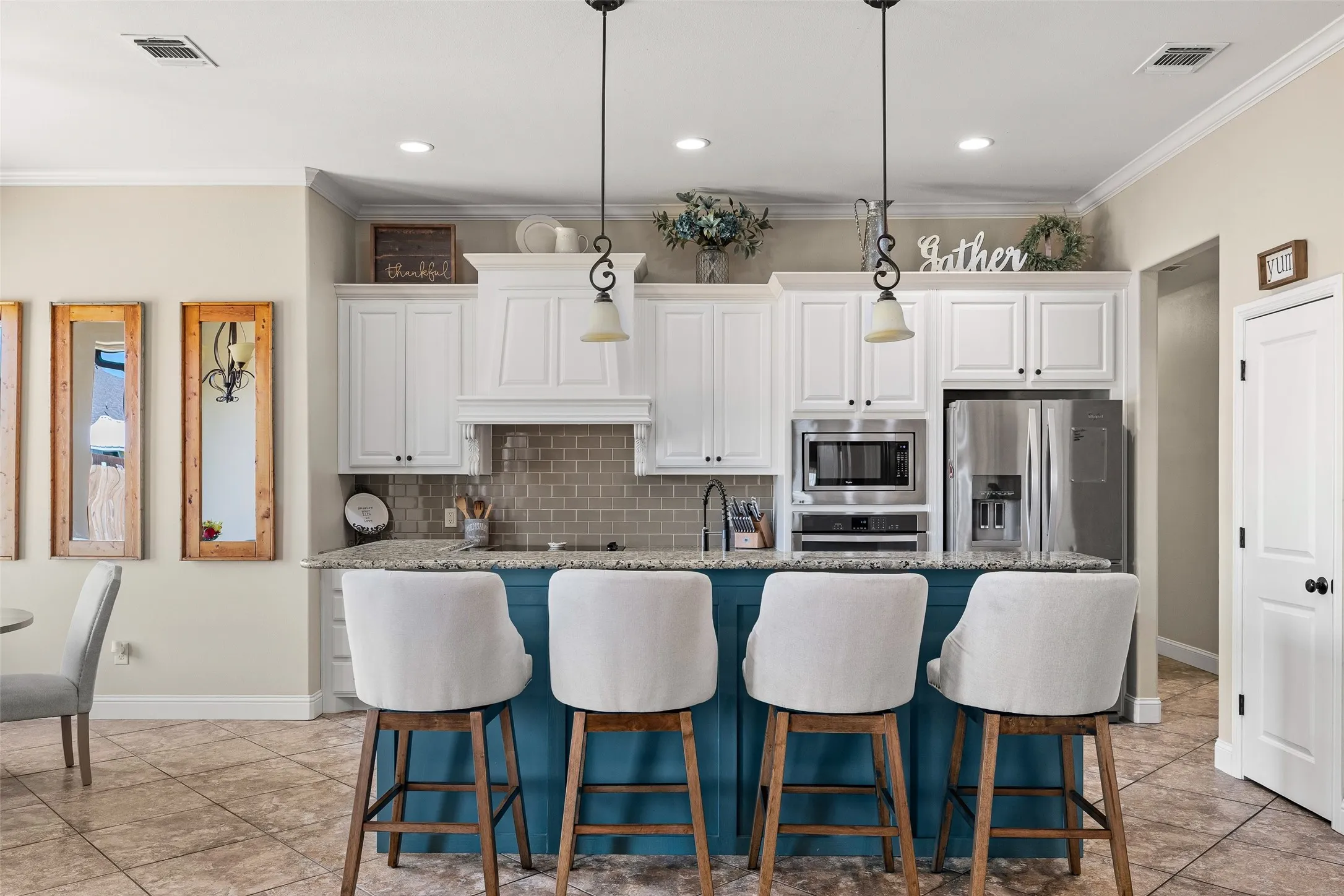 Kitchen featuring a central island with pendant lighting, white cabinetry, integrated stainless steel appliances, a tiled backsplash, and tile flooring
