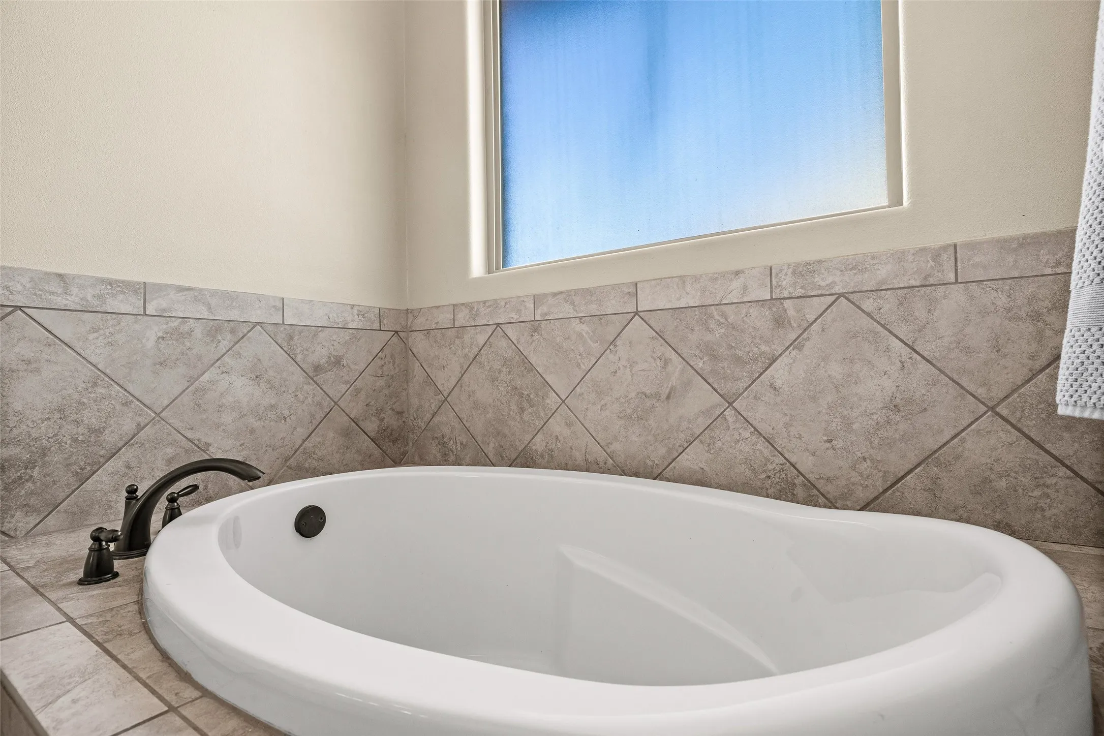 Built-in soaking tub with dark-bronze fixtures, set within a tiled surround featuring a diamond-patterned accent