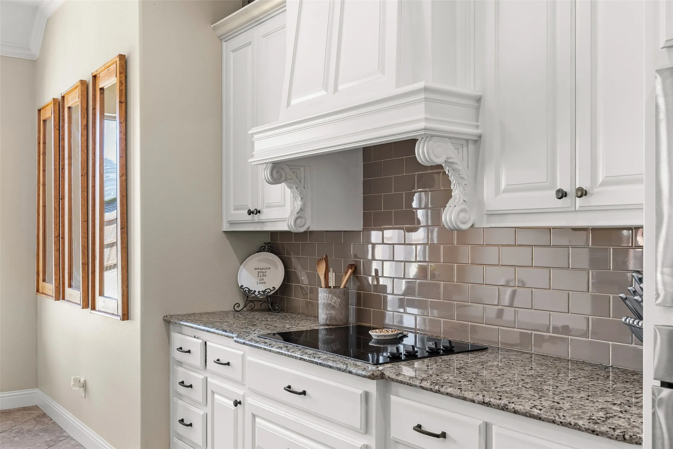 White cabinetry with black hardware, stone-finish countertops, stainless steel cooktop, and subway tile backsplash