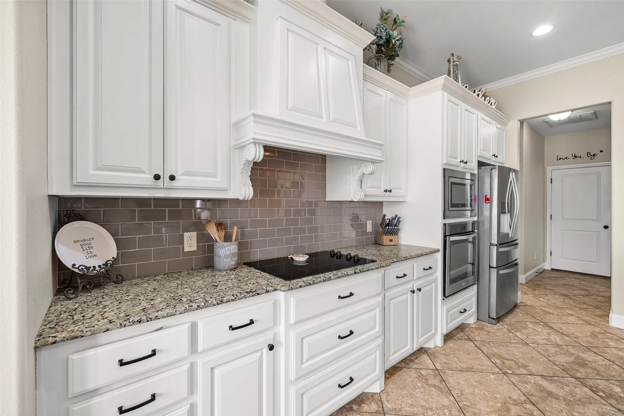 White cabinetry, granite countertops, subway tile backsplash, stainless steel appliances, and tiled flooring