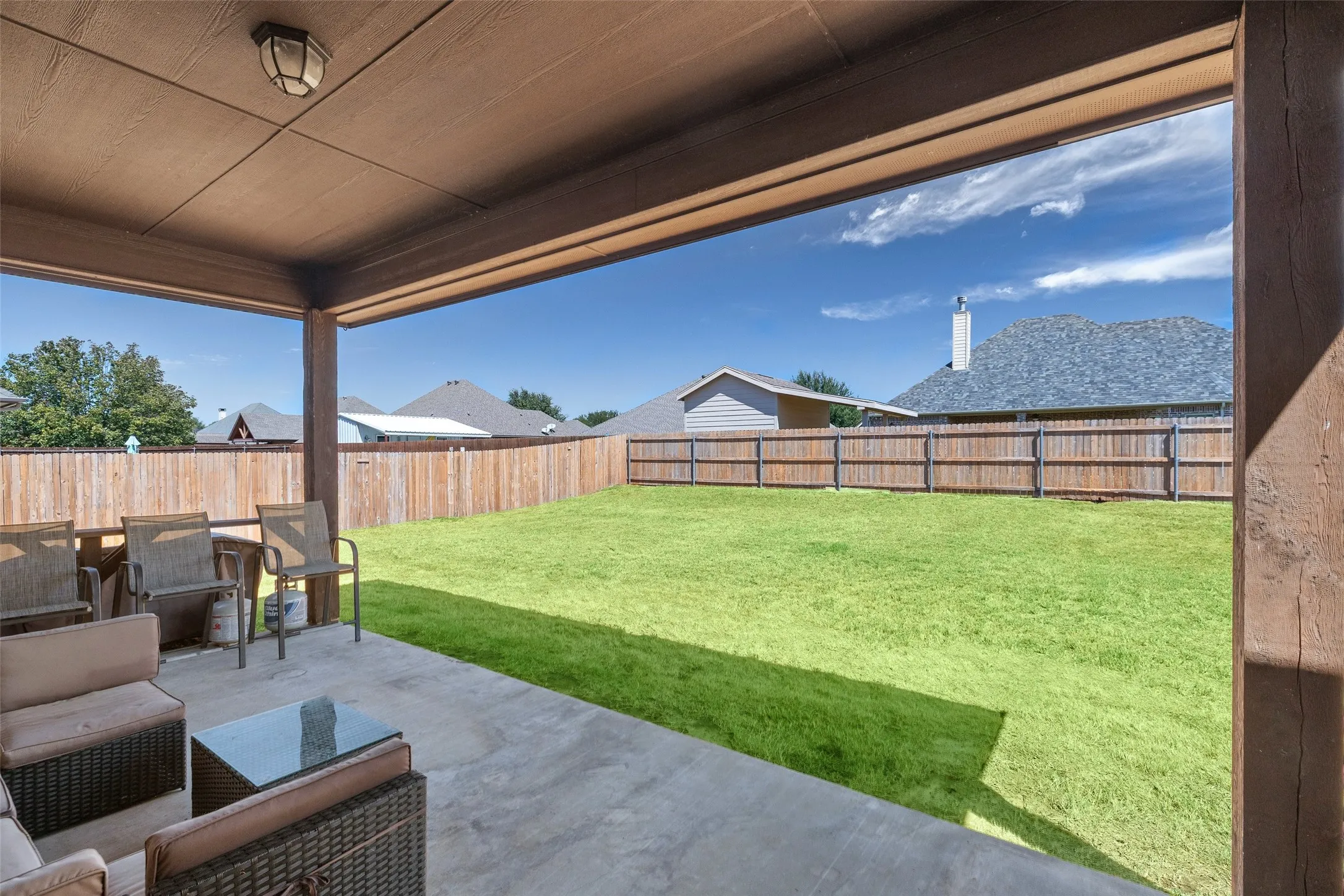 Covered concrete patio with an overhead light fixture, overlooking a fenced yard with a vibrant lawn