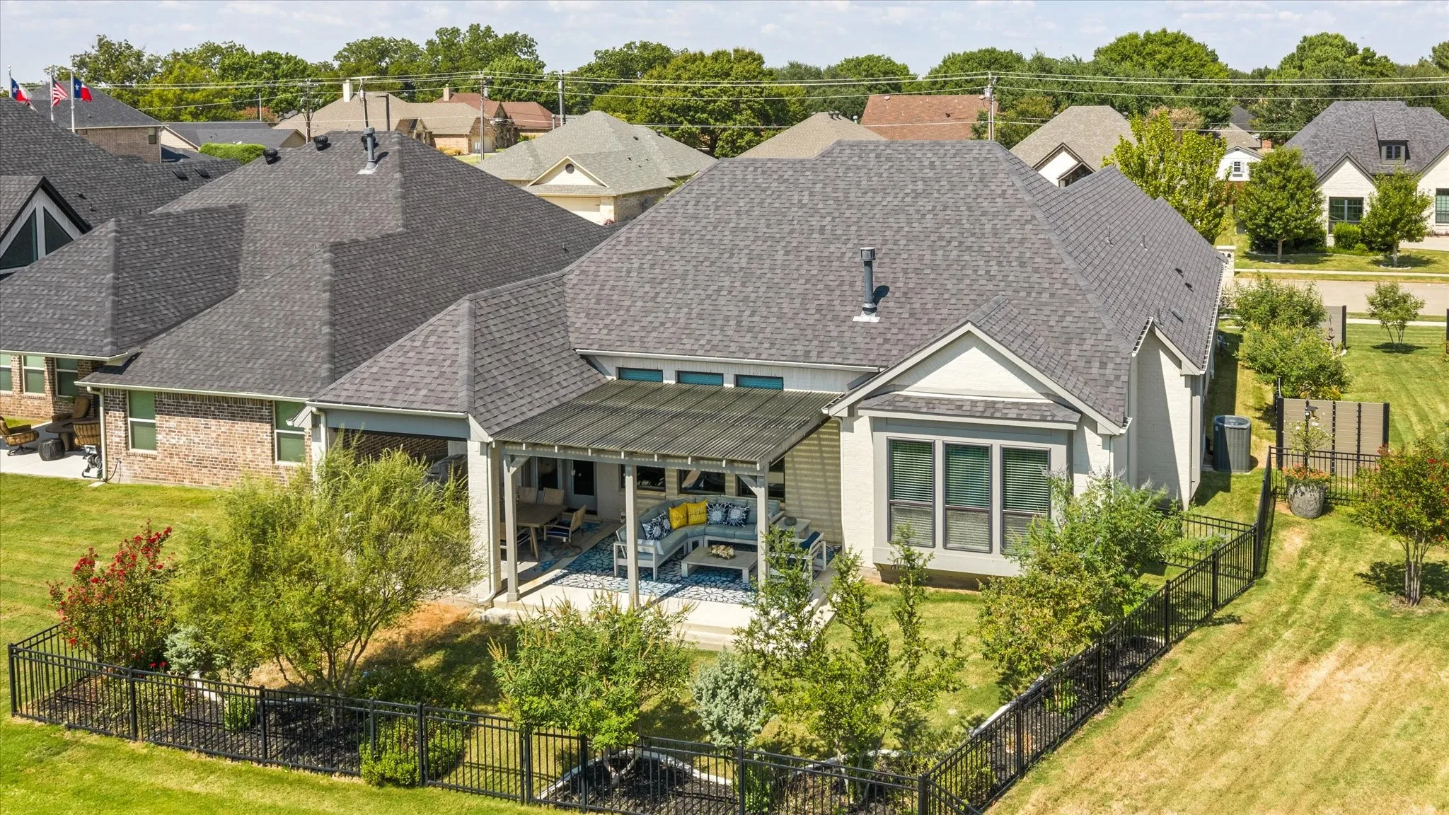 Expansive backyard featuring a covered patio, wrought iron fencing, and mature landscaping