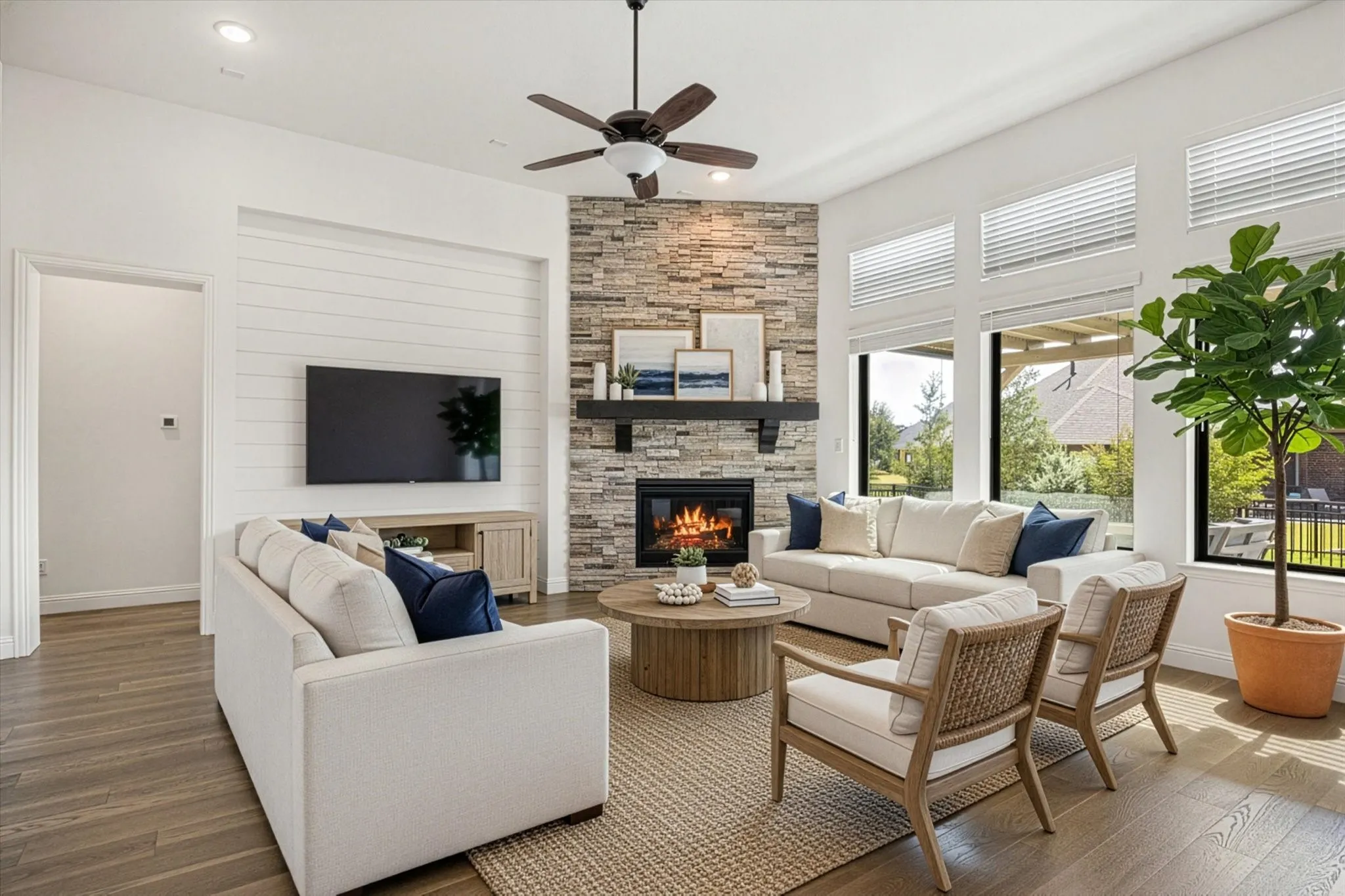 Virtual staging Open-concept living area featuring a stone-clad fireplace, wood-finish flooring, and expansive windows