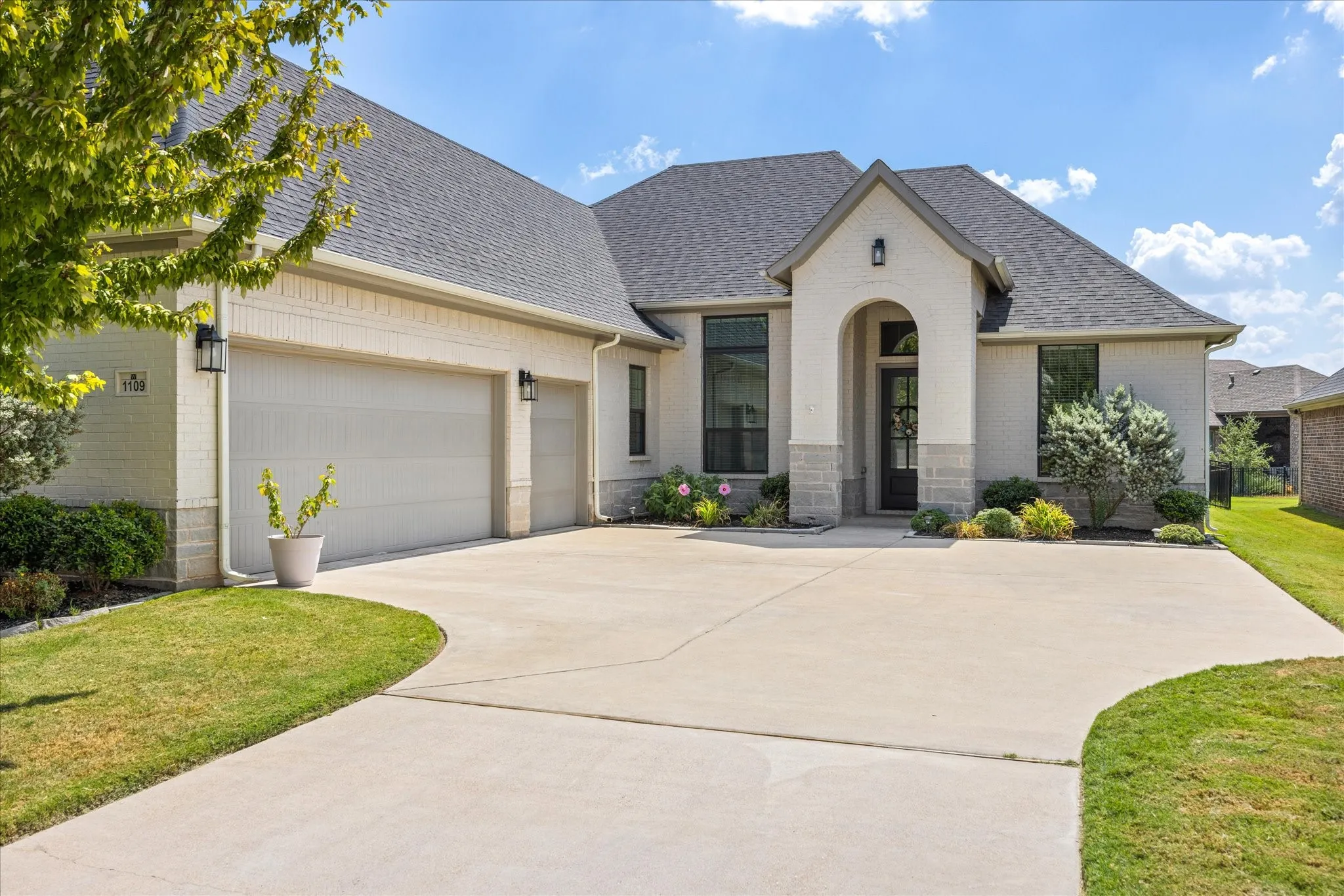 Cream brick exterior with stone accents, dark shingles, an arched entryway, and a concrete driveway