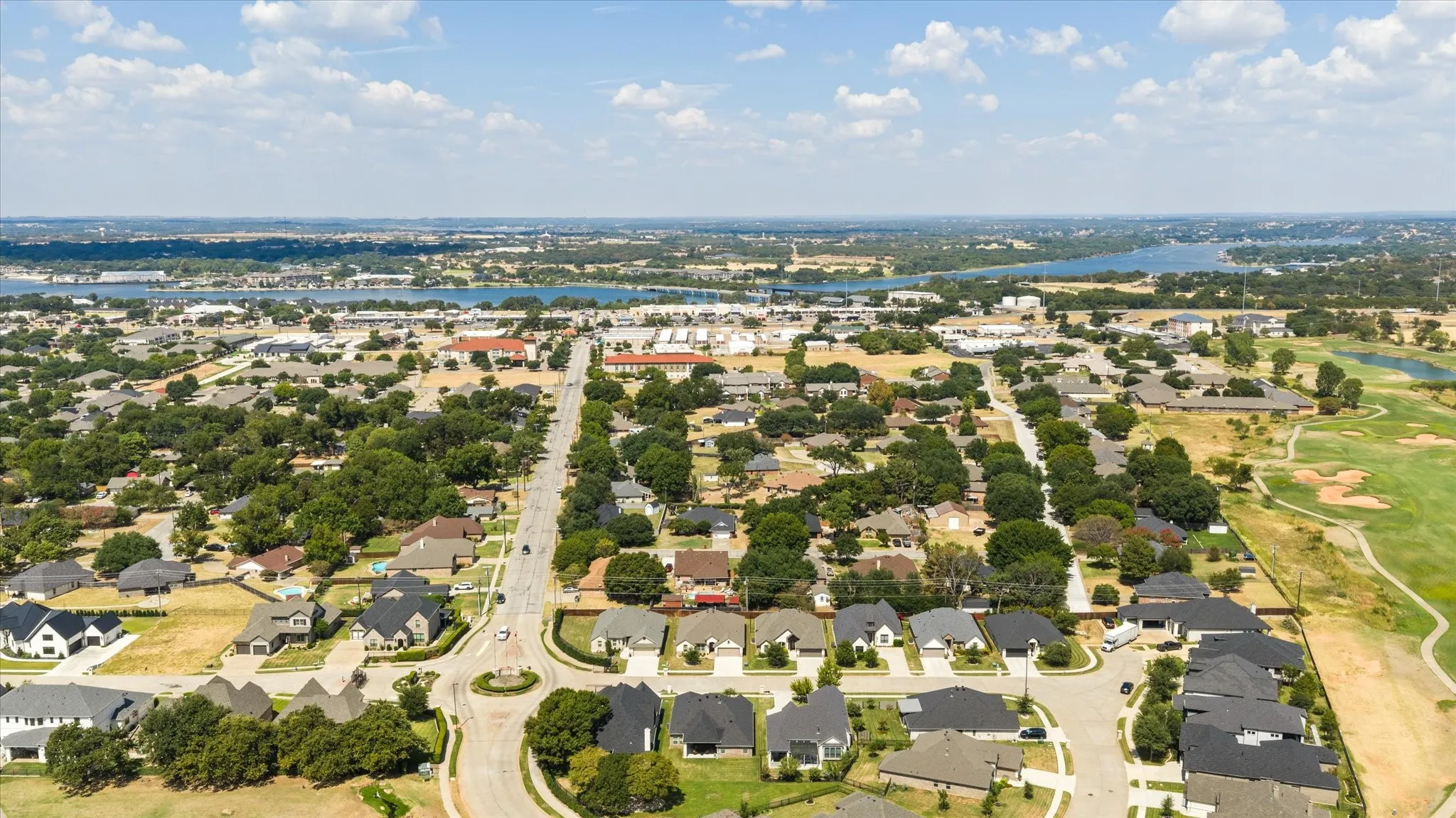Aerial perspective showcasing residential properties, a manicured golf course, and a prominent body of water in the distance