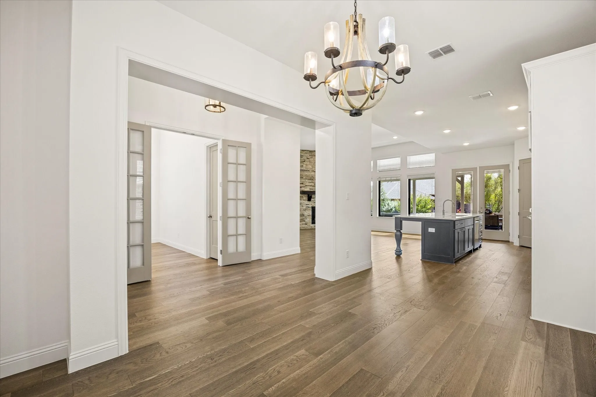 Wood-finish flooring throughout, French doors with glass panels, recessed ceiling lighting, central island with sink, and multiple windows