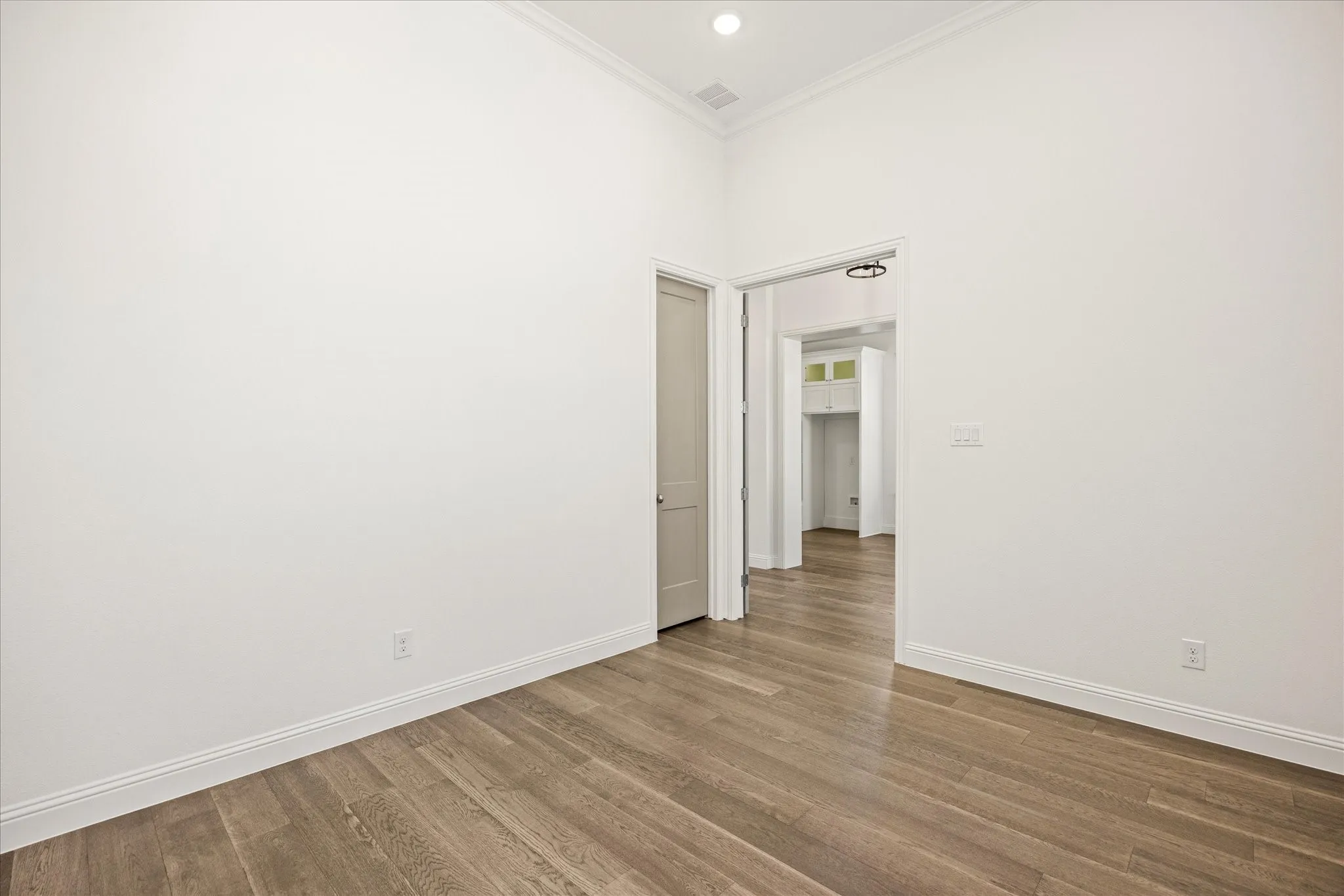 Wood-finish flooring, crisp white walls, recessed lighting, and crown molding