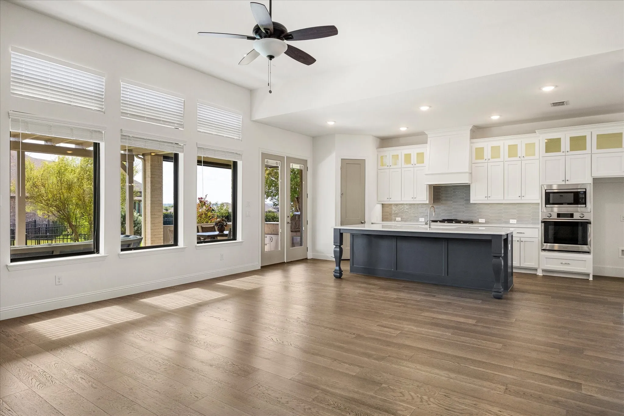 Open-concept living space with wood-finish flooring, a contemporary ceiling fan, and multiple windows