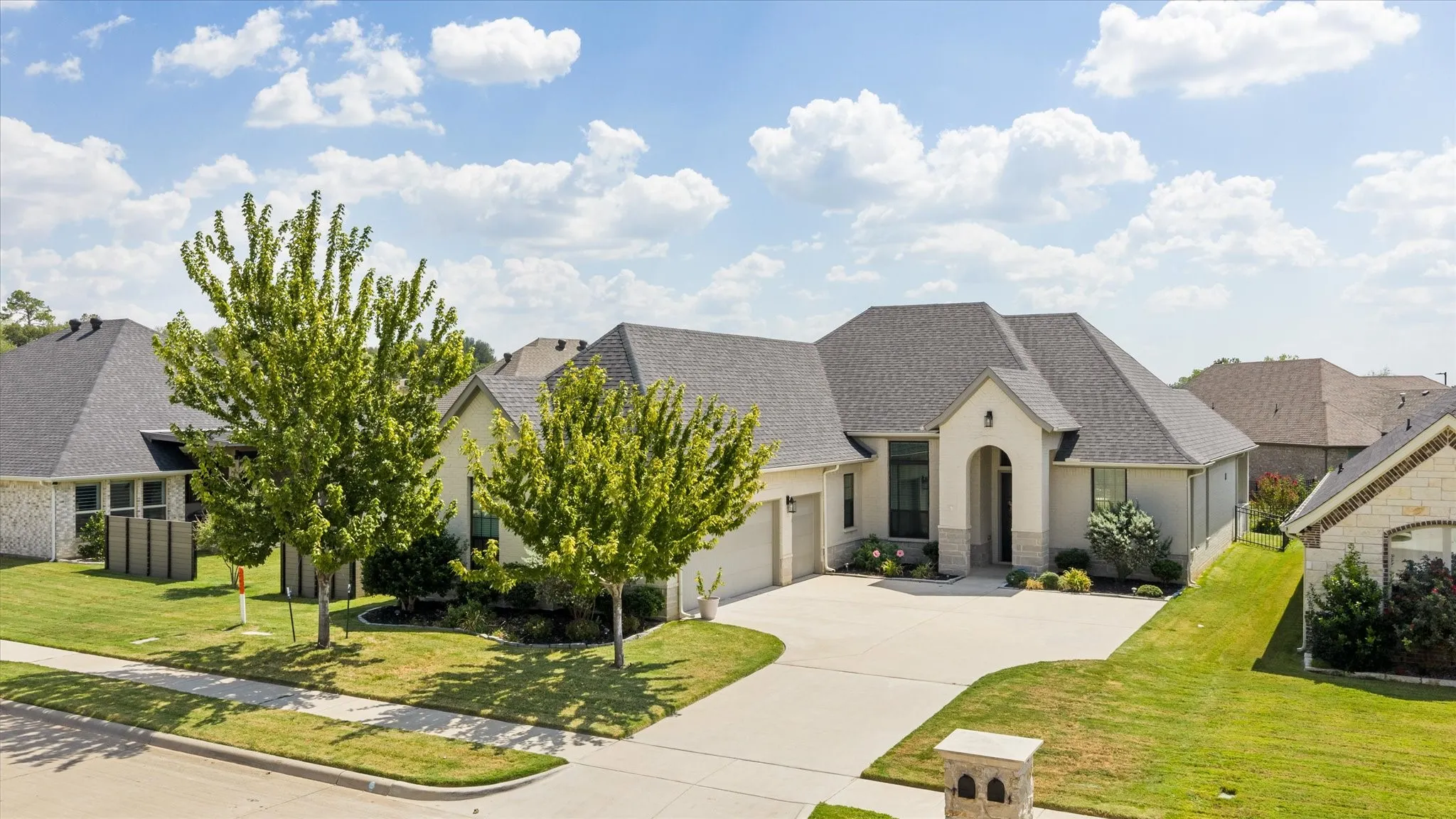 Stucco and stone exterior with an arched entryway, gabled roof, and a paved driveway
