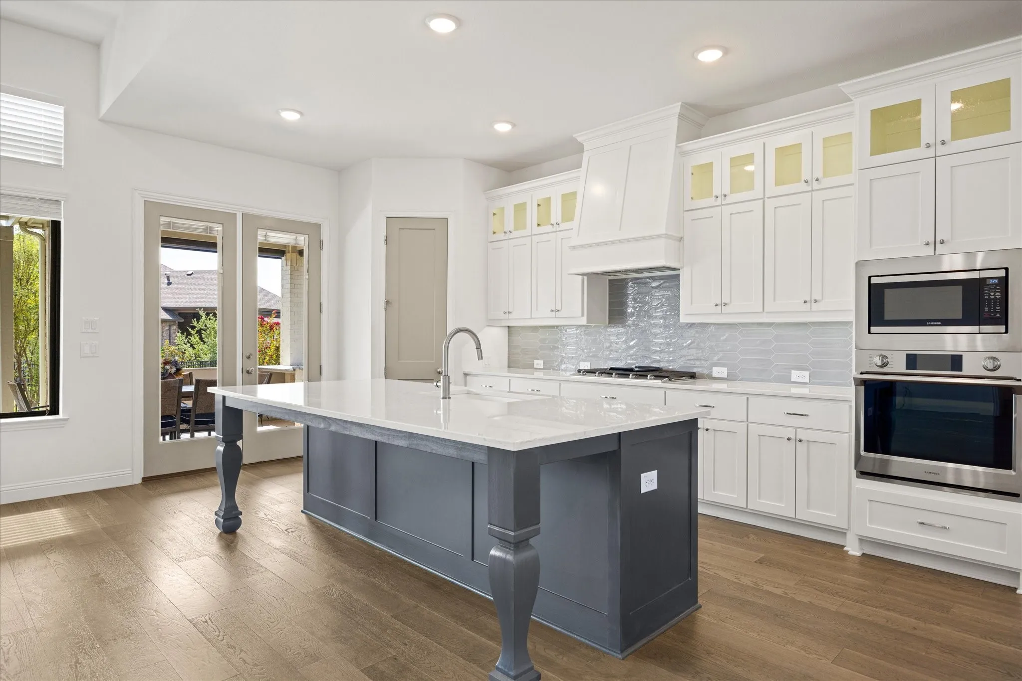 Kitchen featuring a center island with a stone countertop, wood-finish flooring, white cabinetry, a built-in oven, and French doors