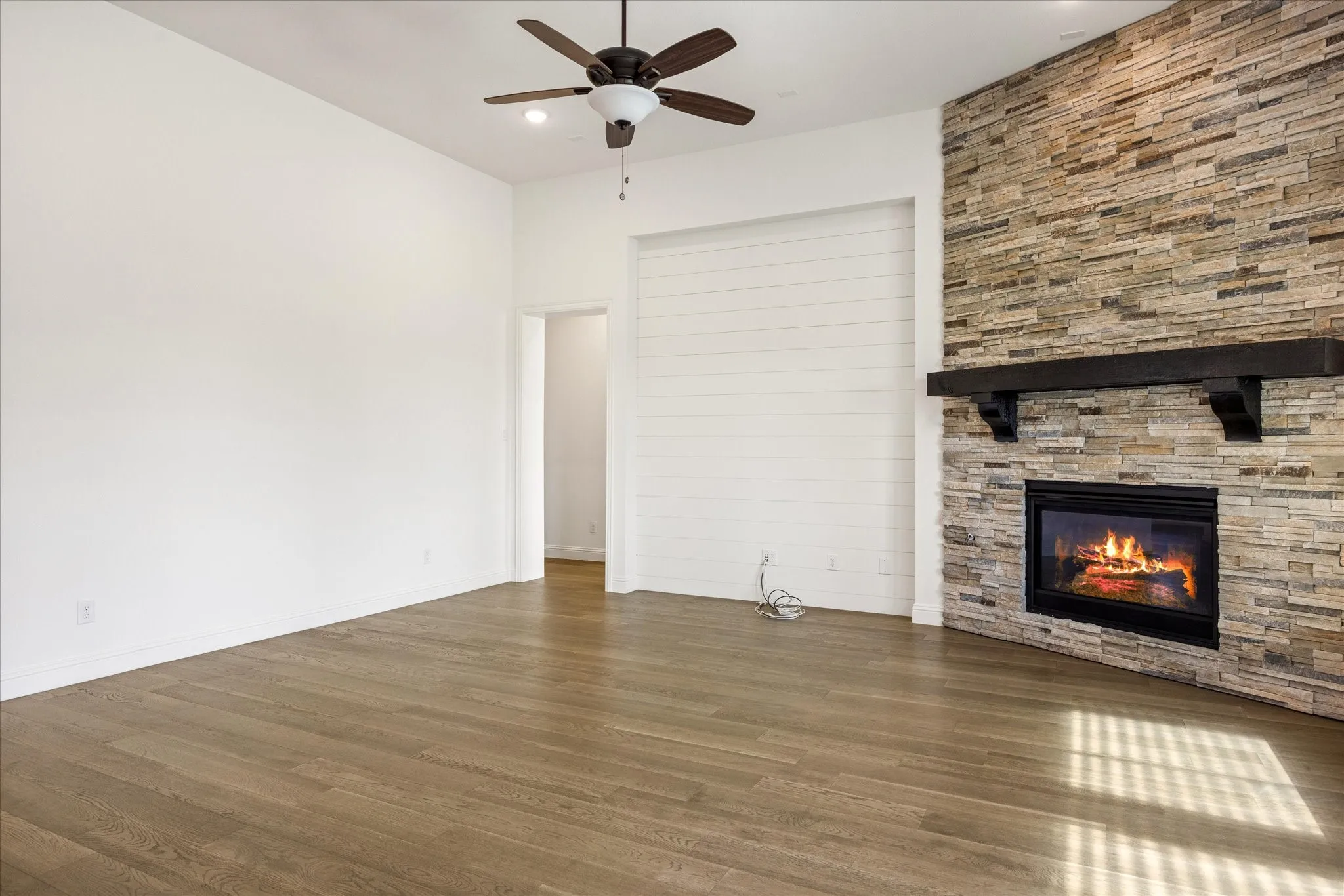 Wood-finish flooring, stone-clad fireplace with a dark wood mantle, integrated fireplace, ceiling fan, and recessed lighting