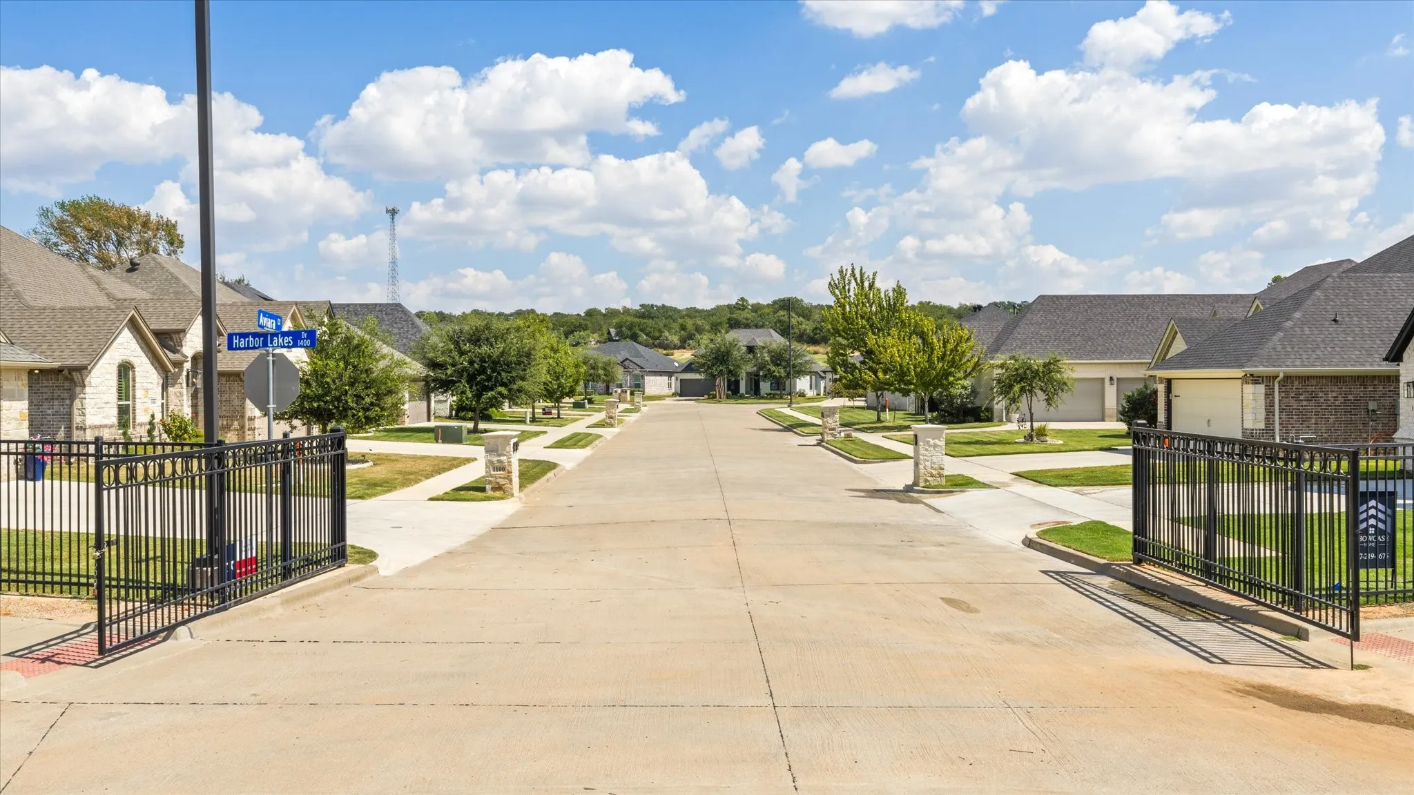 Gated community entrance with asphalt paving and mature landscaping