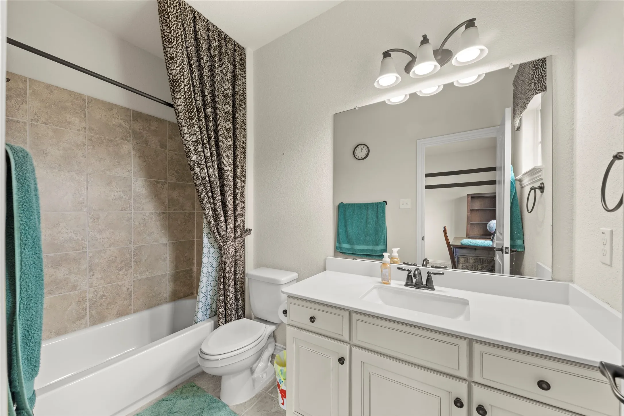 Bathroom featuring a white vanity with an integrated sink, a large mirror, and a three-light fixture