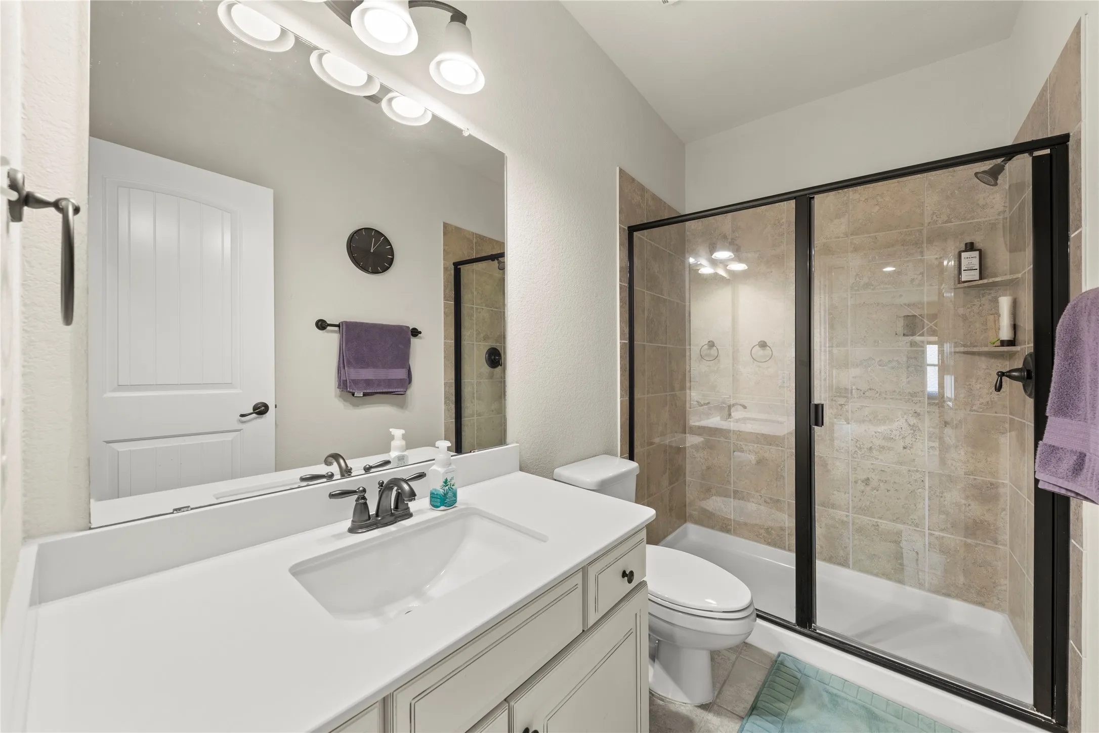 Full bathroom featuring a shower with glass enclosure, large format wall tiling, a built-in shower niche, a single vanity with an integrated sink, and an overhead vanity light fixture