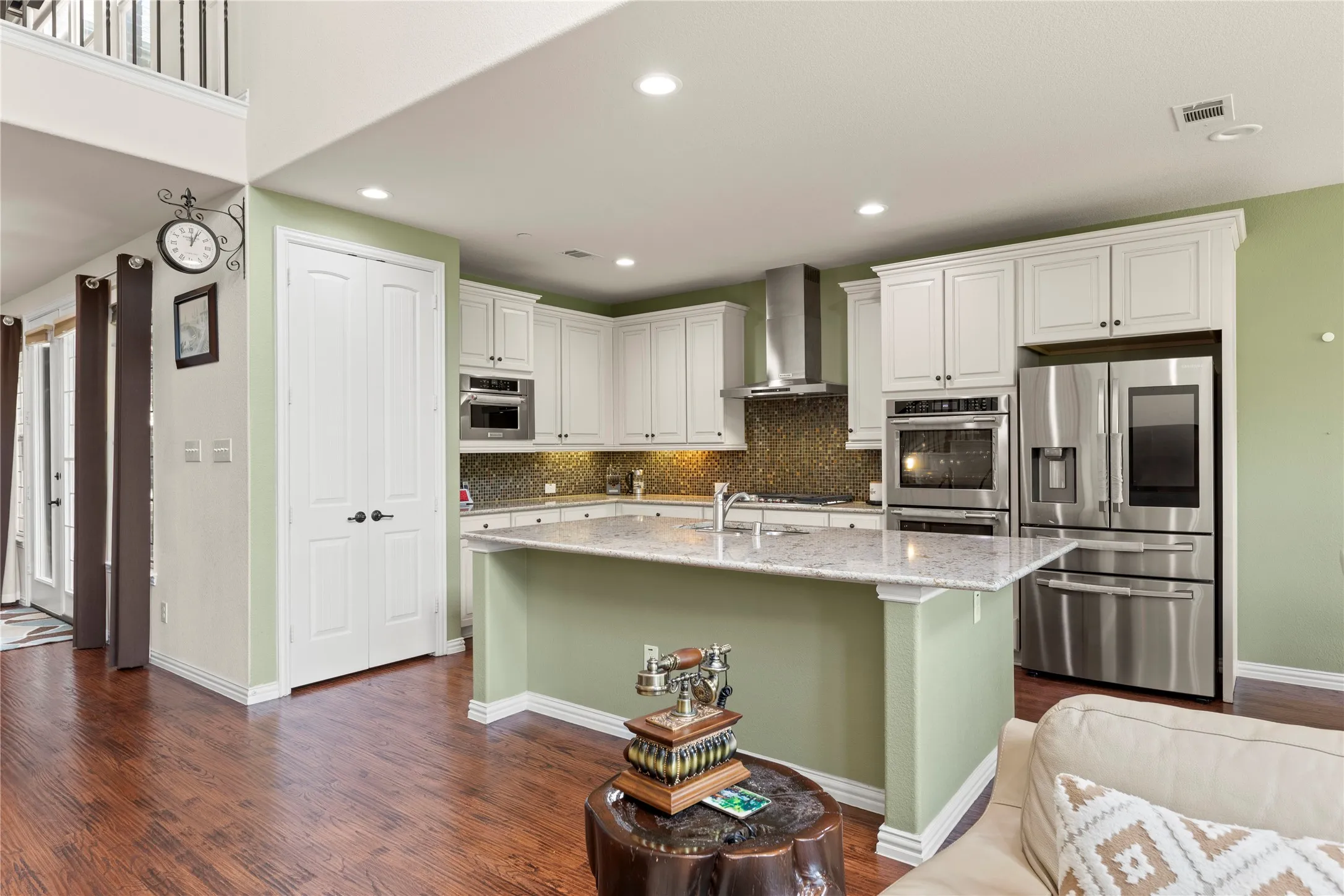 Modern kitchen featuring white cabinetry, stainless steel appliances, a textured tile backsplash, an island with a light-toned countertop, and wood-finish flooring