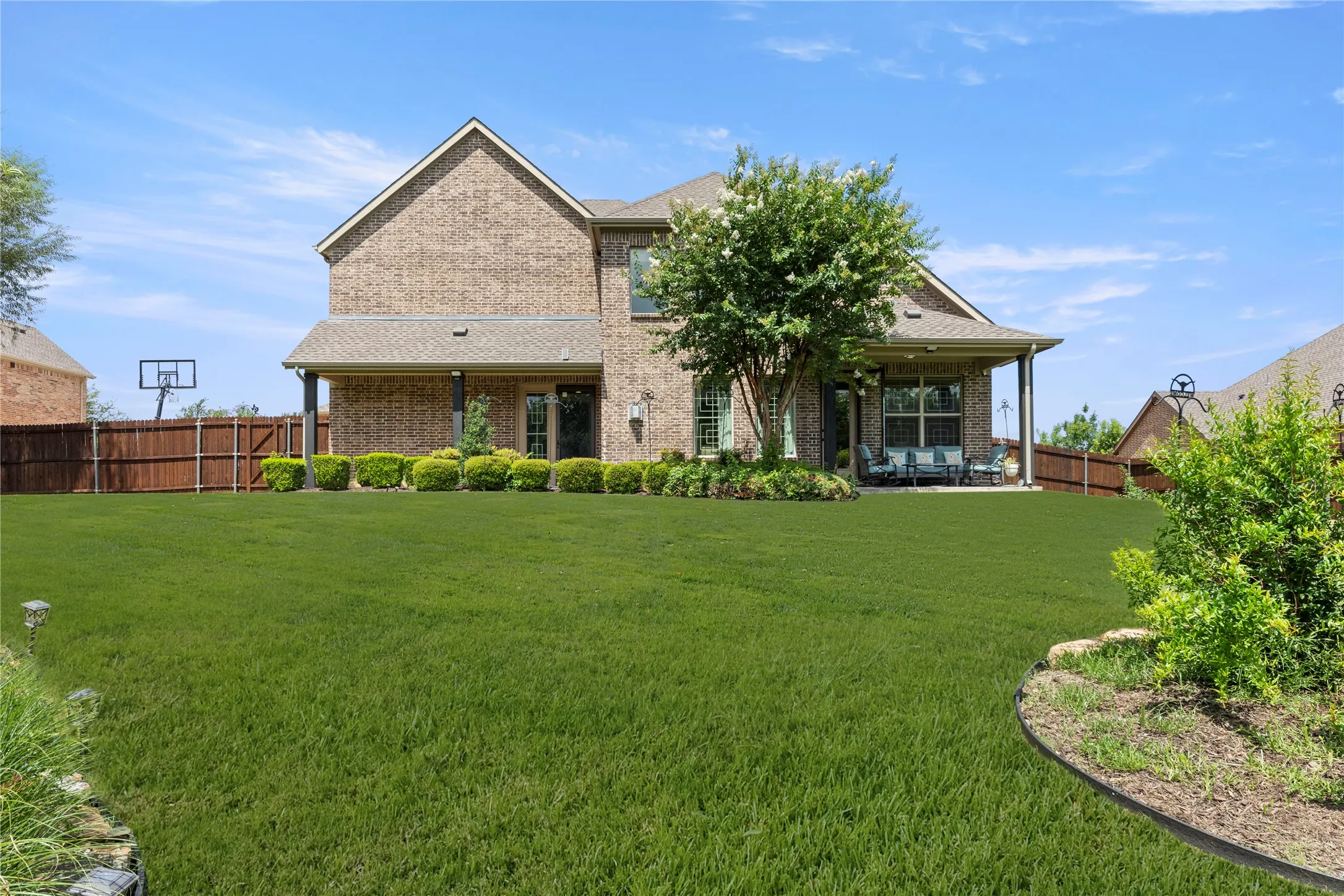Expansive backyard featuring a lush lawn, a covered patio, and mature landscaping